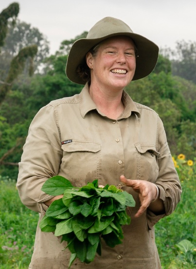 Lisa Hill wearing a ranger hat and shirt, smiling. In the background is native forest