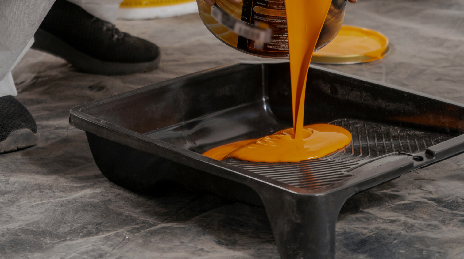 Person pouring orange paint into a black tray