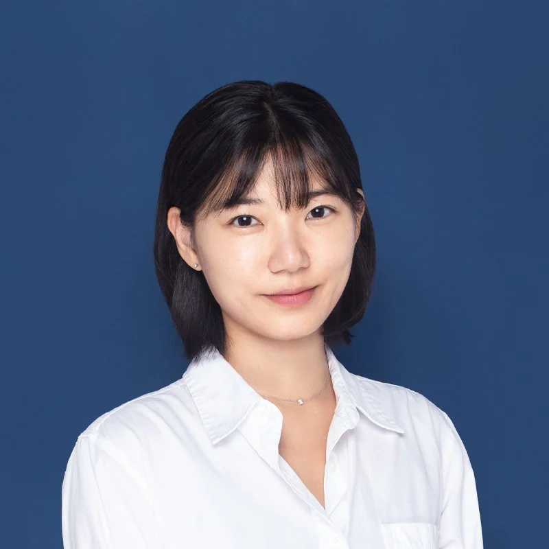 Professional headshot of Dr. Seohyun Joo: Short-haired androgynous woman in a white shirt, against a dark blue background. 짙은 파란색 배경과 숏컷 스타일이 돋보이는 주서현 박사의 메인 프로필 사진.
