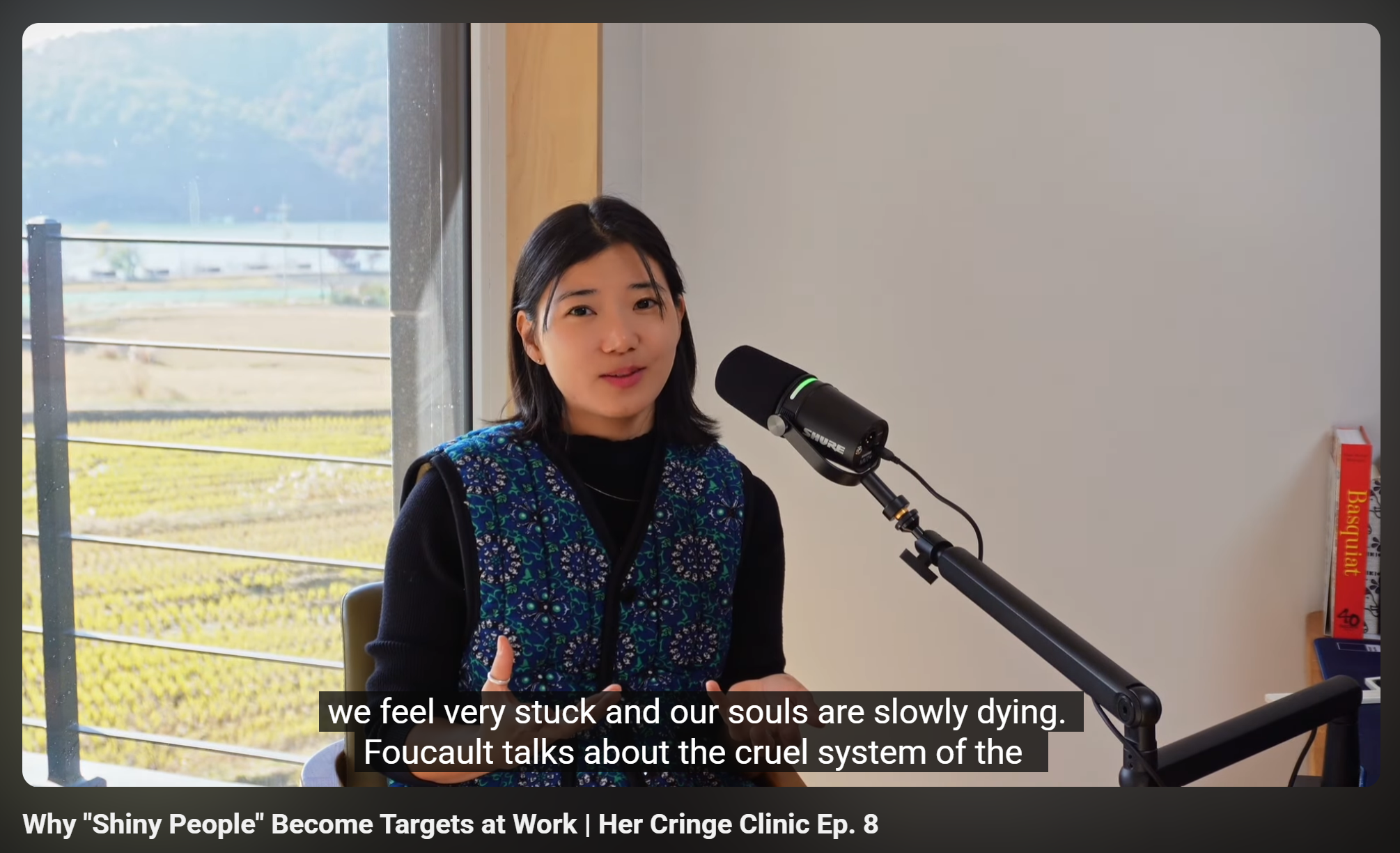 Dr. Seohyun Joo with shoulder-length black hair, wearing a traditional Korean padded vest (Kimjang vest), speaking into a microphone. Discussing Foucault and how society traps us like prisons. 한국 전통 누빔 조끼(김장 조끼)를 입고 푸코의 사회 구조론과 직장 내 역동을 설명하는 주서현 박사.