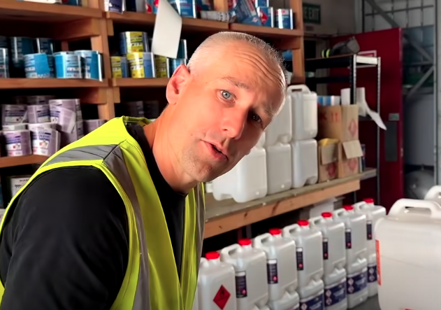 A man wearing a yellow safety vest inside a store aisle with shelves stocked with paint supplies and chemicals.