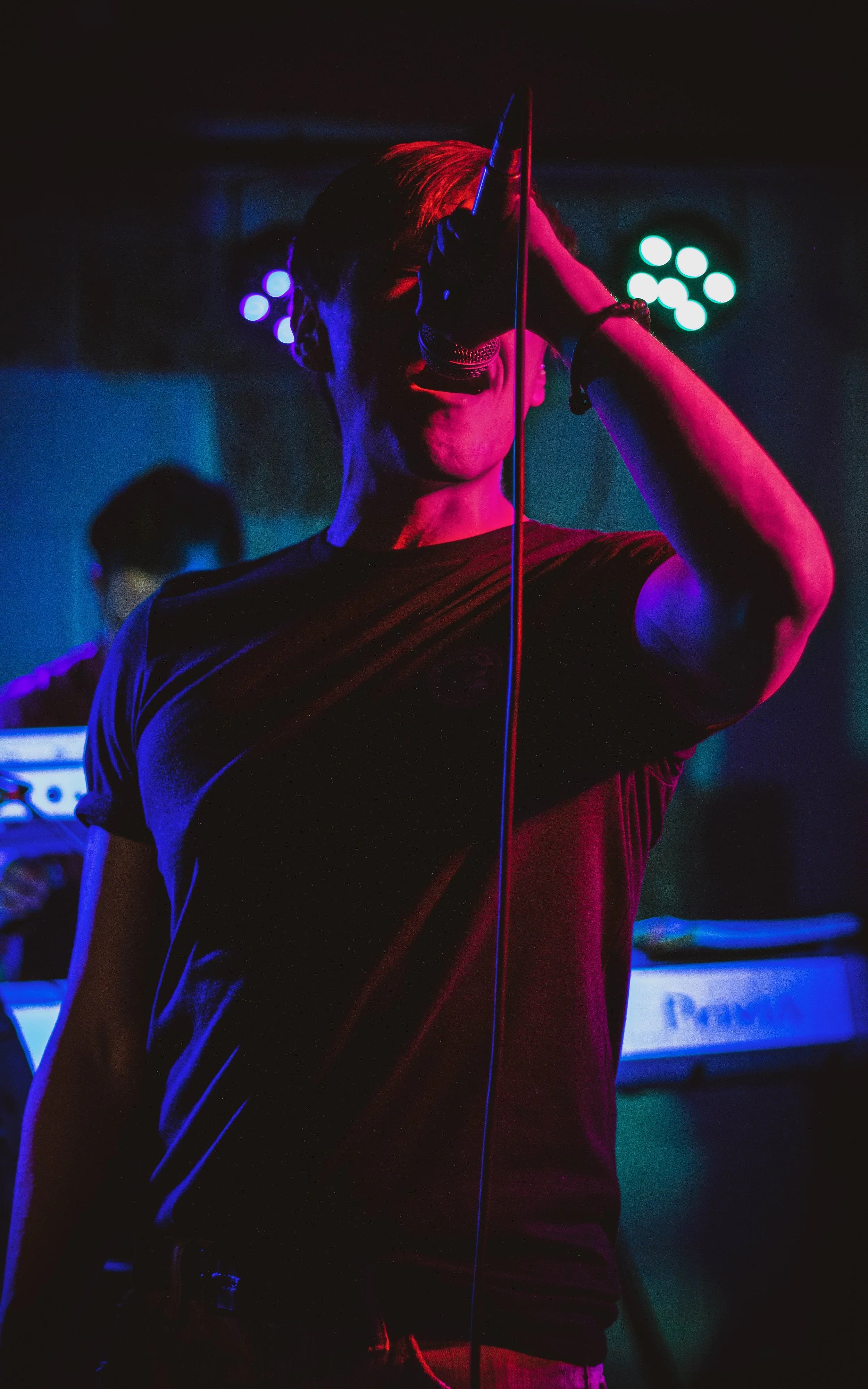 Joven cantando con micrófono en un escenario oscuro iluminado con luces de colores.