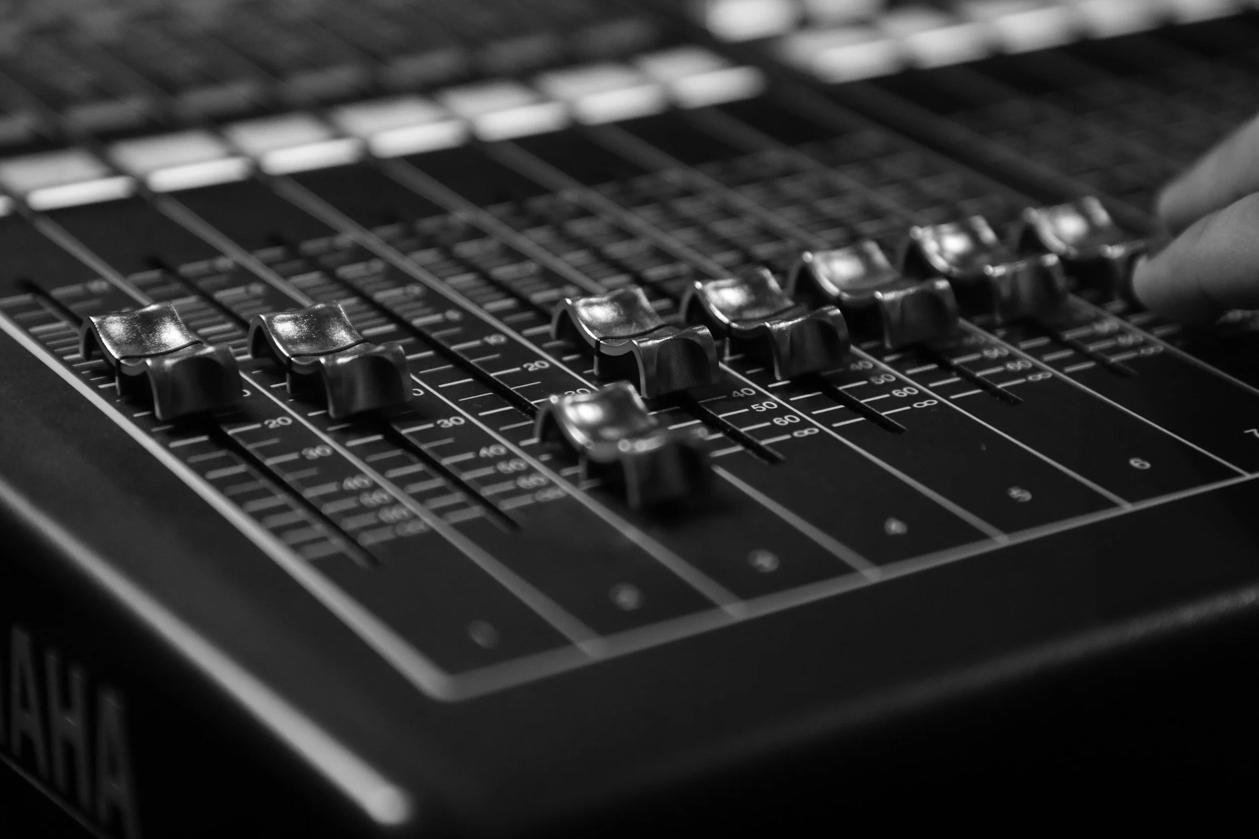 Mezcladora de audio con controles deslizantes y perilla, vista en primer plano en blanco y negro.