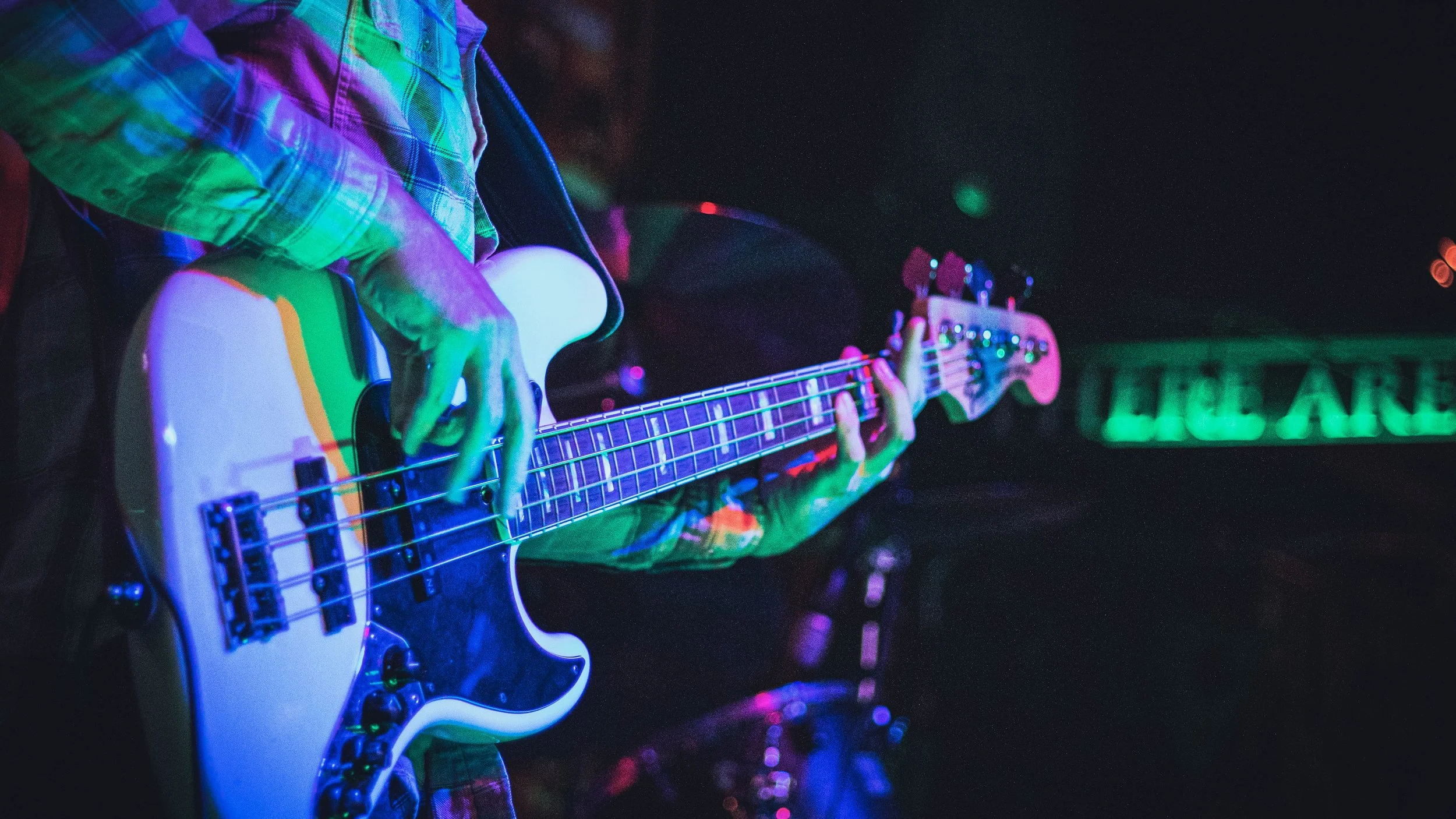 Persona tocando un bajo en un escenario con iluminación de colores.