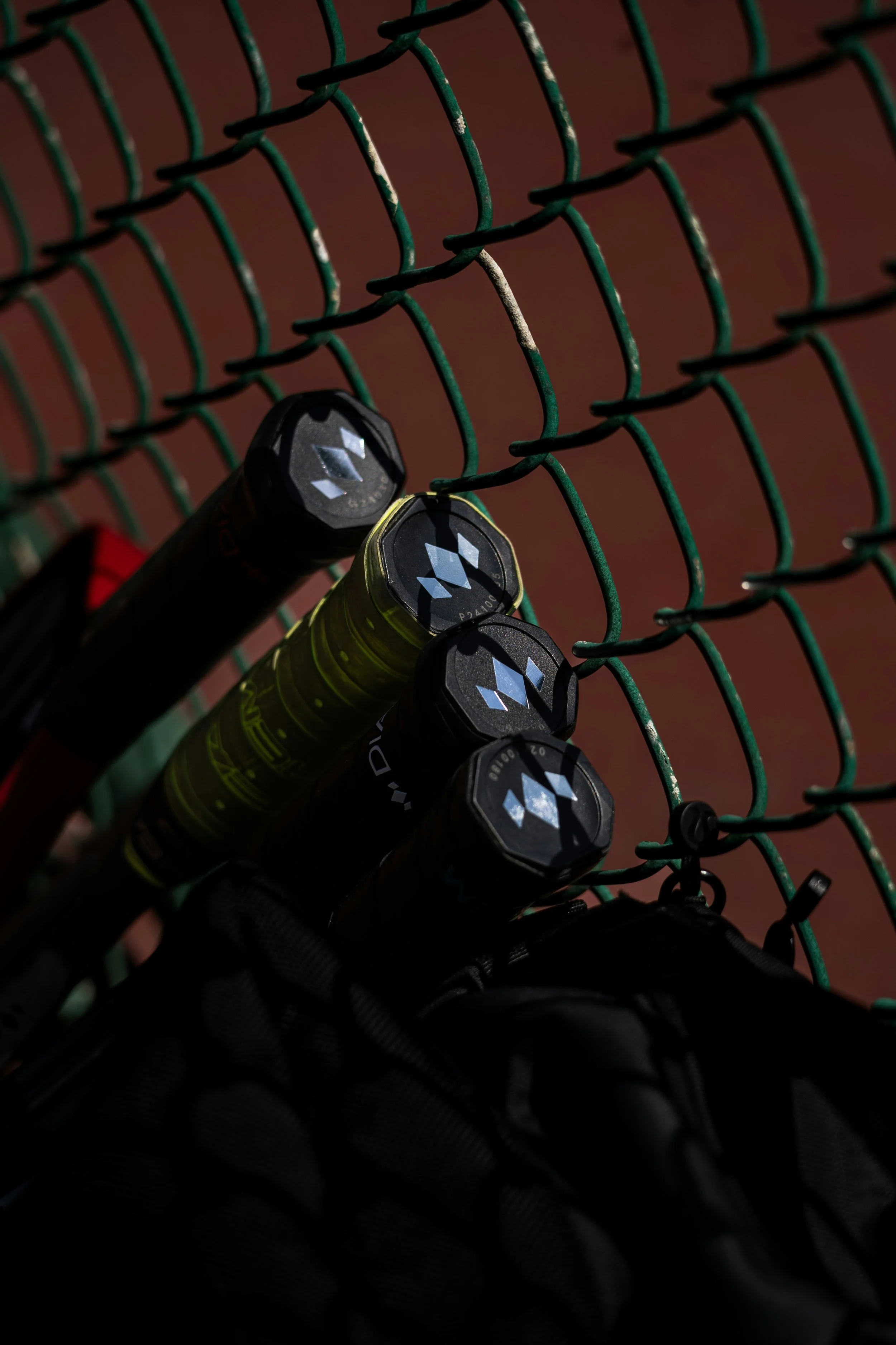 Close-up of tennis rackets and a bag hanging on a green chain-link fence at a tennis court.