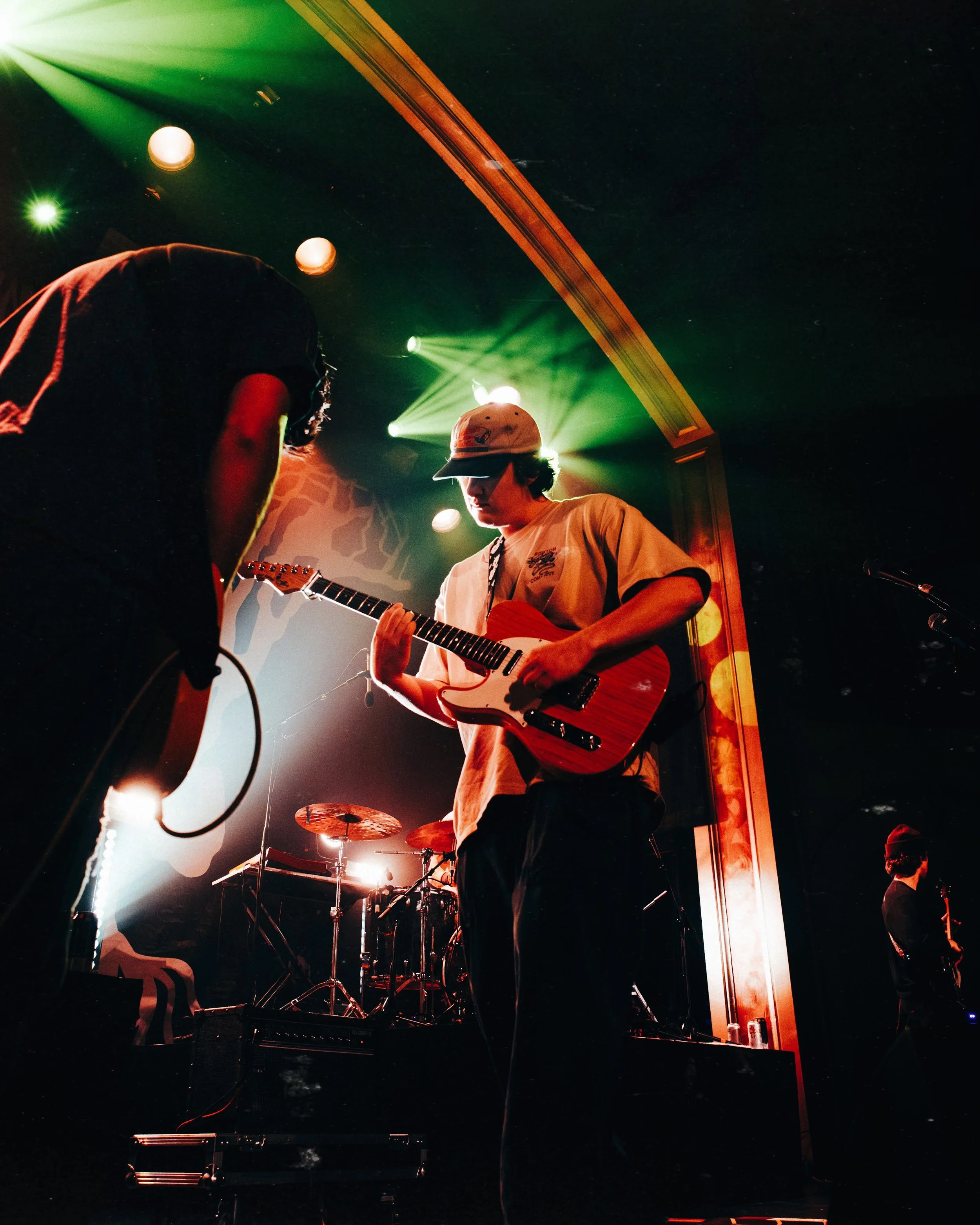 Musicians performing on stage with colorful lights and drum set in the background.