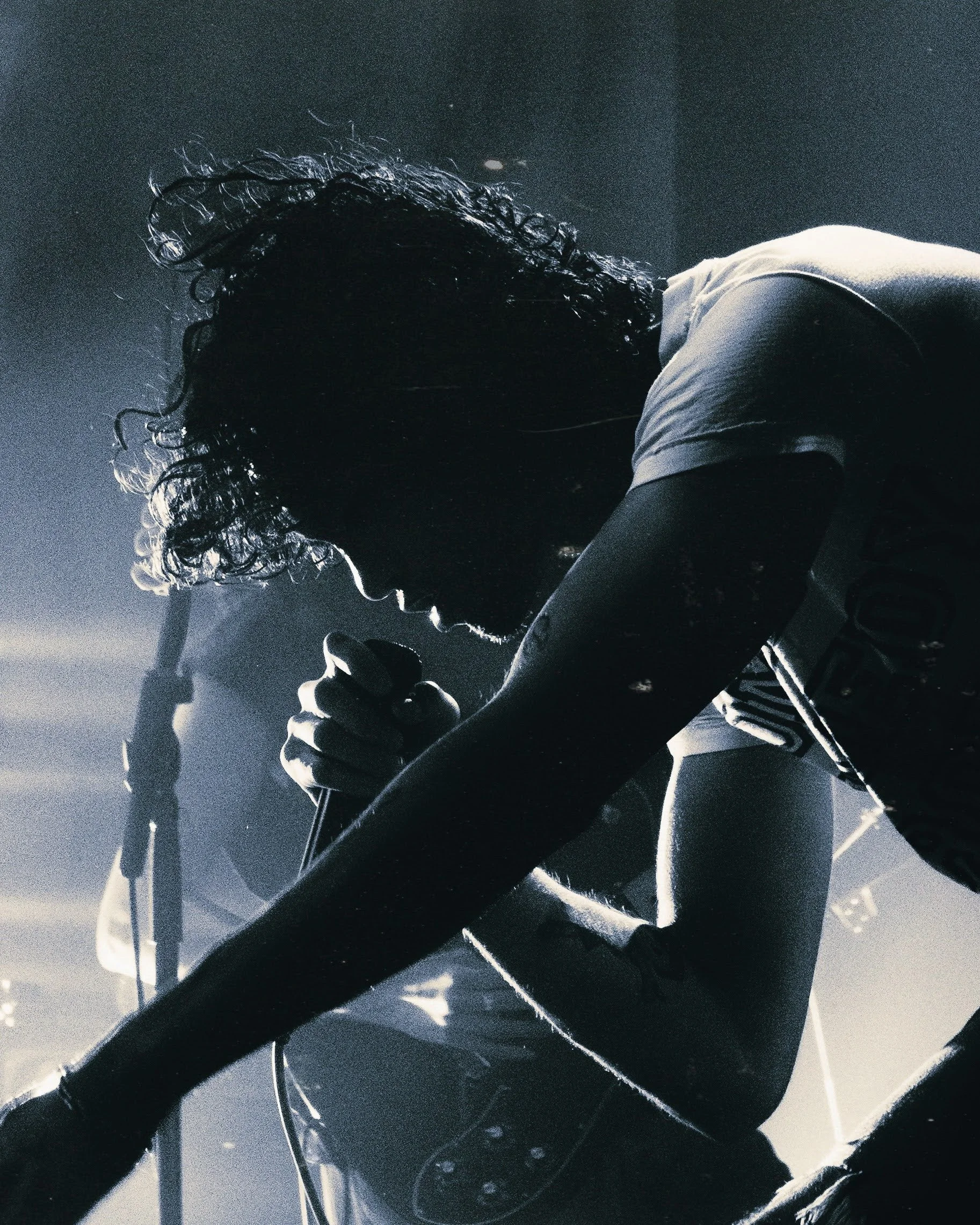 Silhouette of a musician with curly hair singing into a microphone with stage lights in the background.