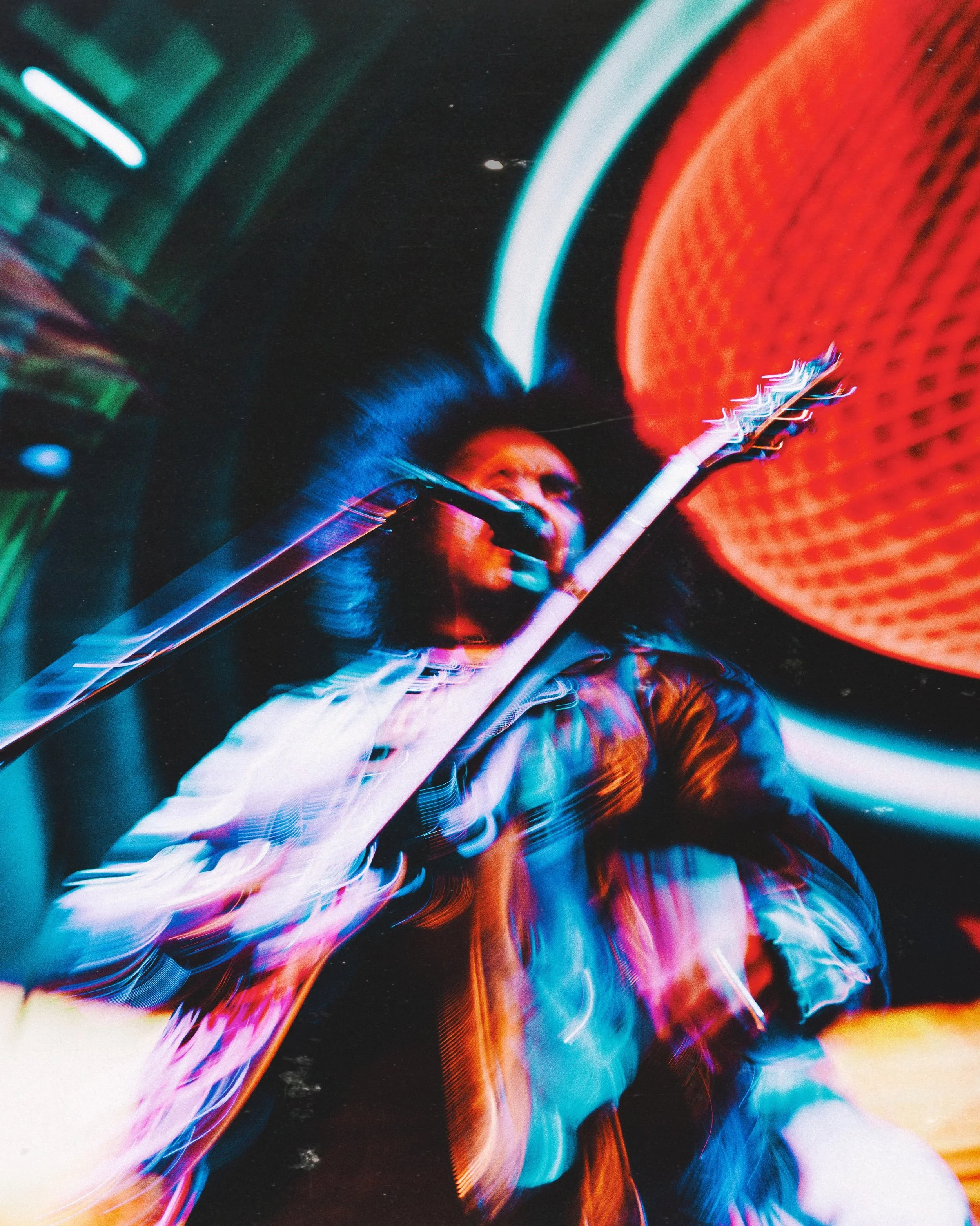 A person playing an electric guitar amidst vibrant, neon-colored lights at a night event or concert.