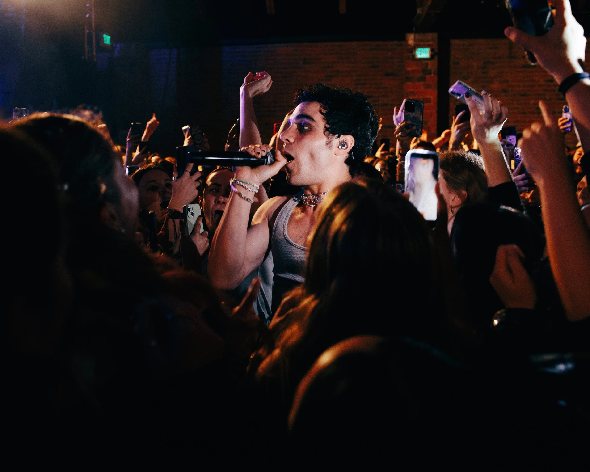 Singer performing at a concert with a crowd holding up phones and taking photos.