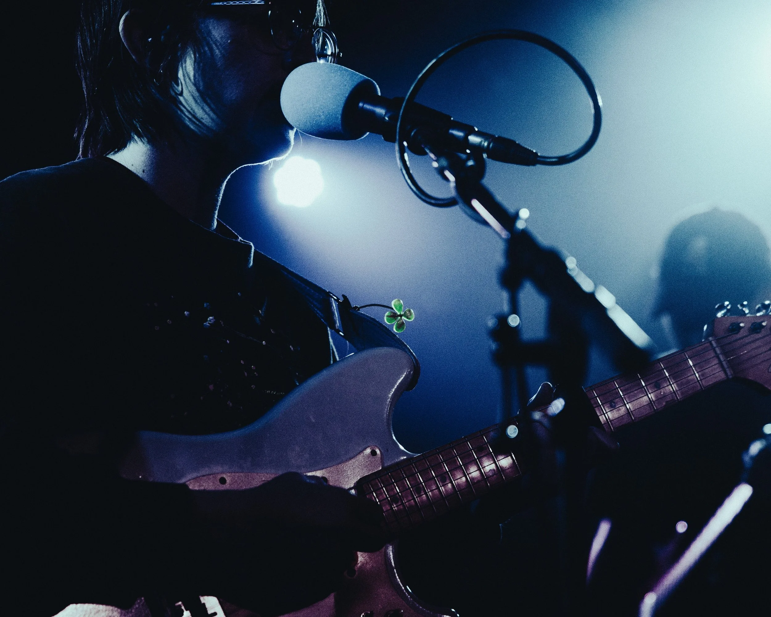 Musician performing with an electric guitar and microphone on stage with blue lighting.