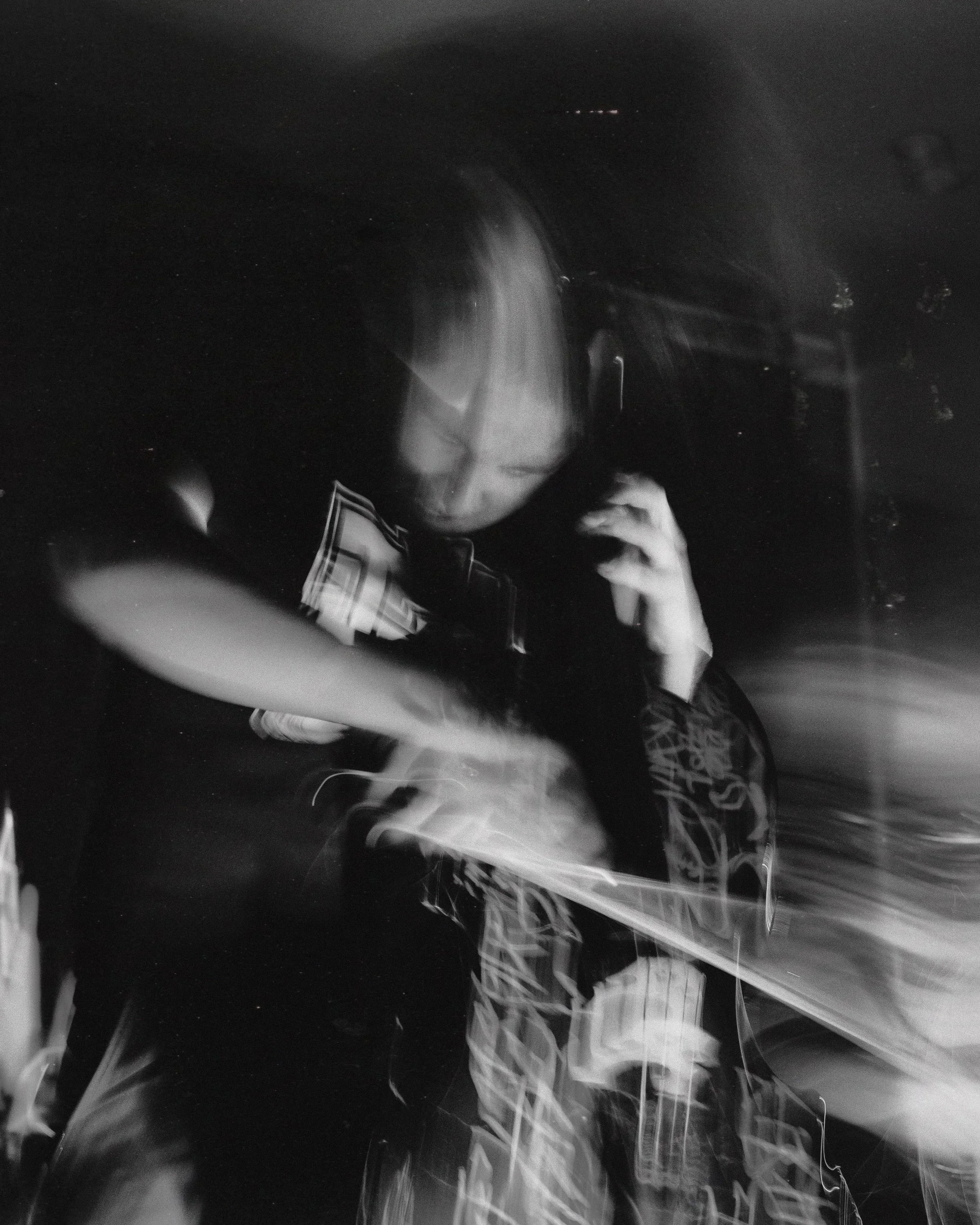 A black and white, blurry photo of a person with blonde hair talking on a phone, with motion streaks creating a feeling of movement.