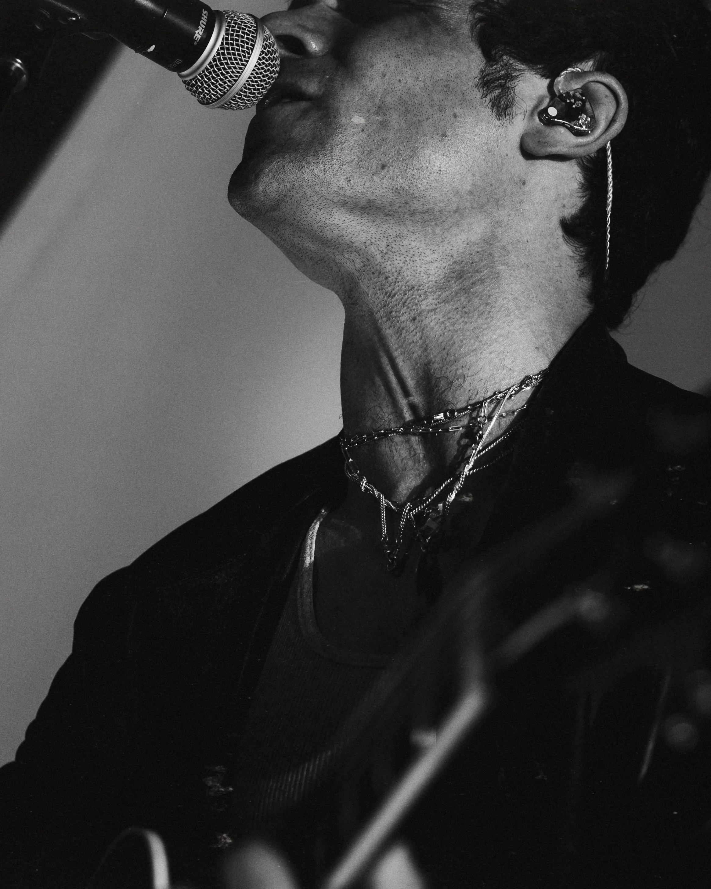 A black and white photo of a person singing into a microphone, wearing jewelry and an earpiece.