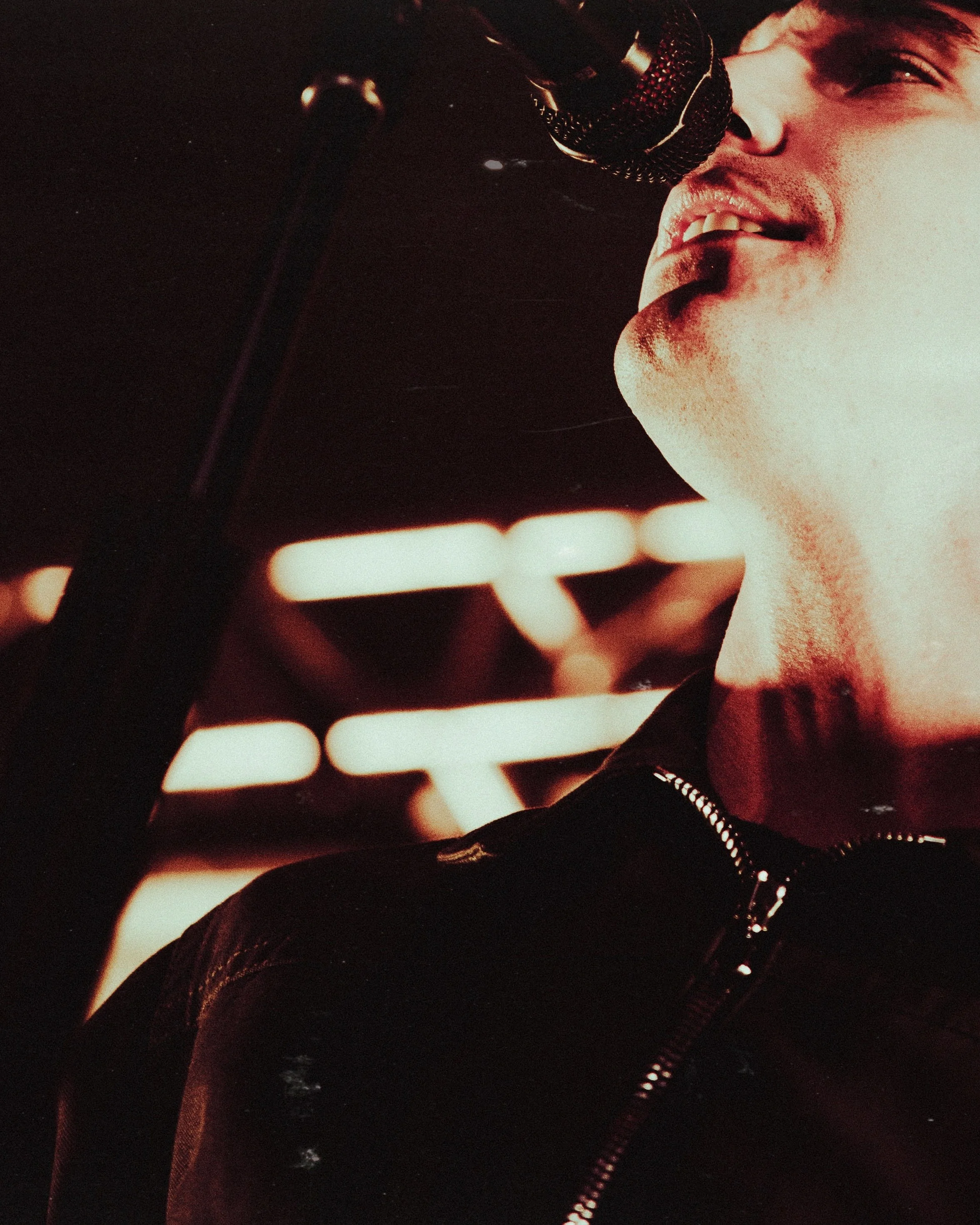 A person singing into a microphone with neon lights in the background.