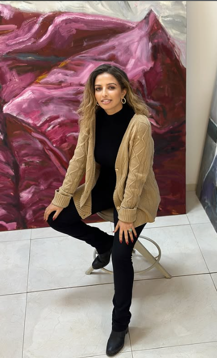 Femme assise sur une chaise devant une peinture abstraite rose et violette.