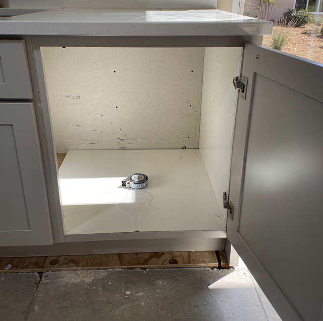 new dishwasher unboxed beside open sink cabinet