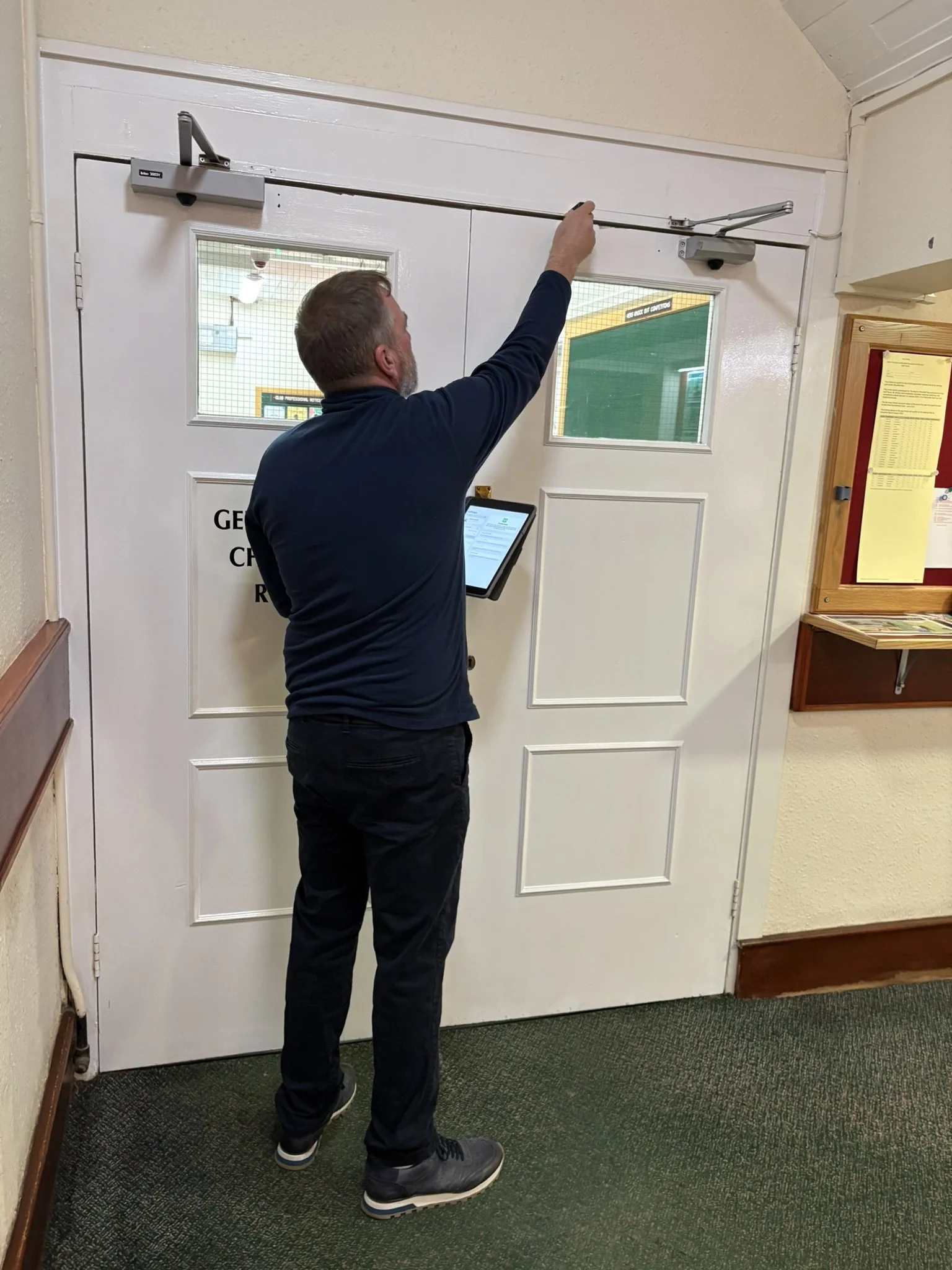 A man with a tablet in his left hand is completing a fire door survey.
