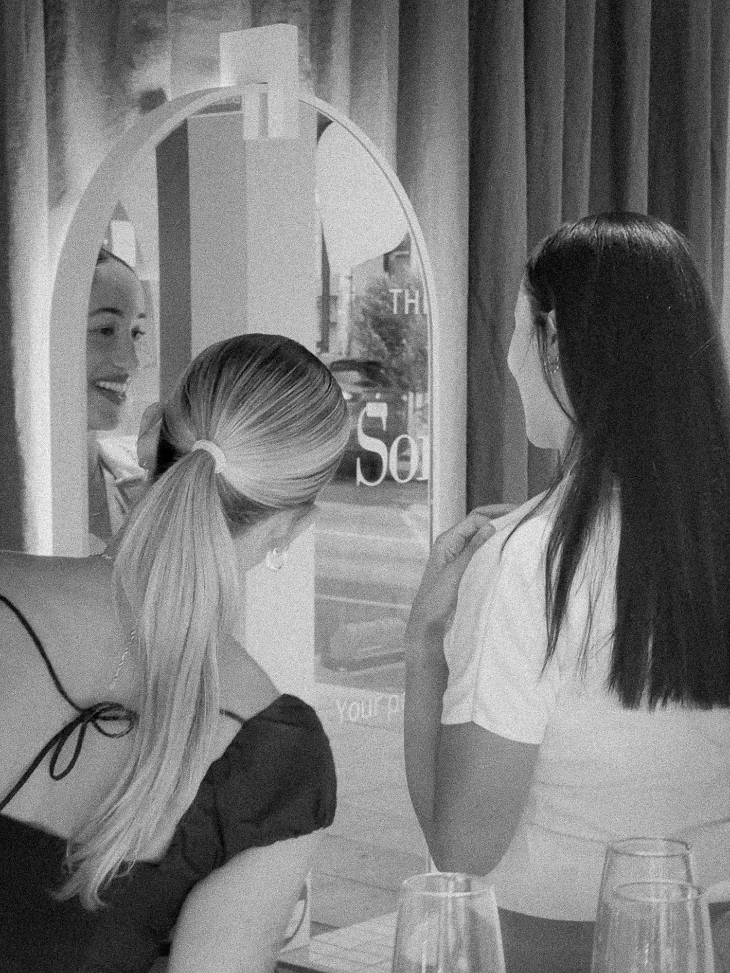 woman looking in mirror smiling as she tries on a necklace shop assistant looking on