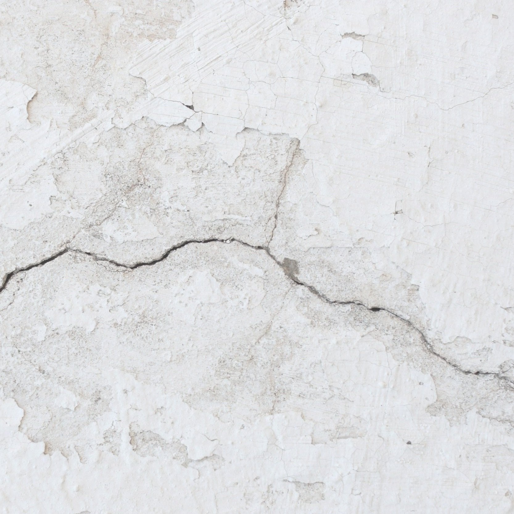 Close-up of a cracked and peeling white wall surface.