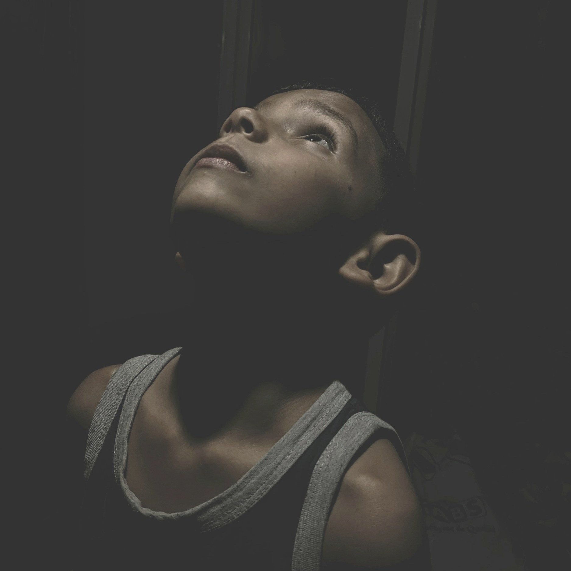 A young boy looking upward with shadows obscuring most of his face and part of his clothing.