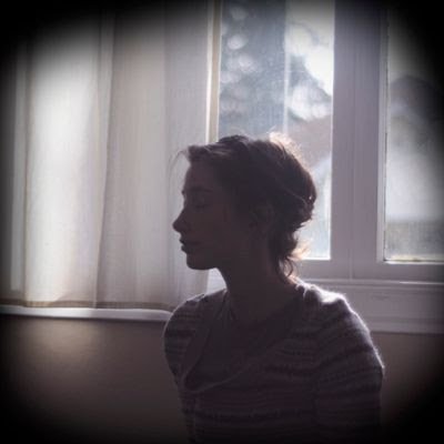 Silhouette of a woman with curly hair sitting by a window with curtains, backlit by daylight.
