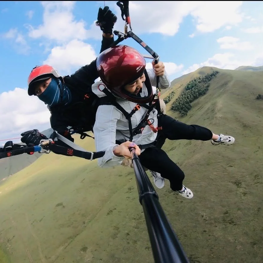 Tsogoo flying a tandem paraglider with a passenger over green Mongolian hills