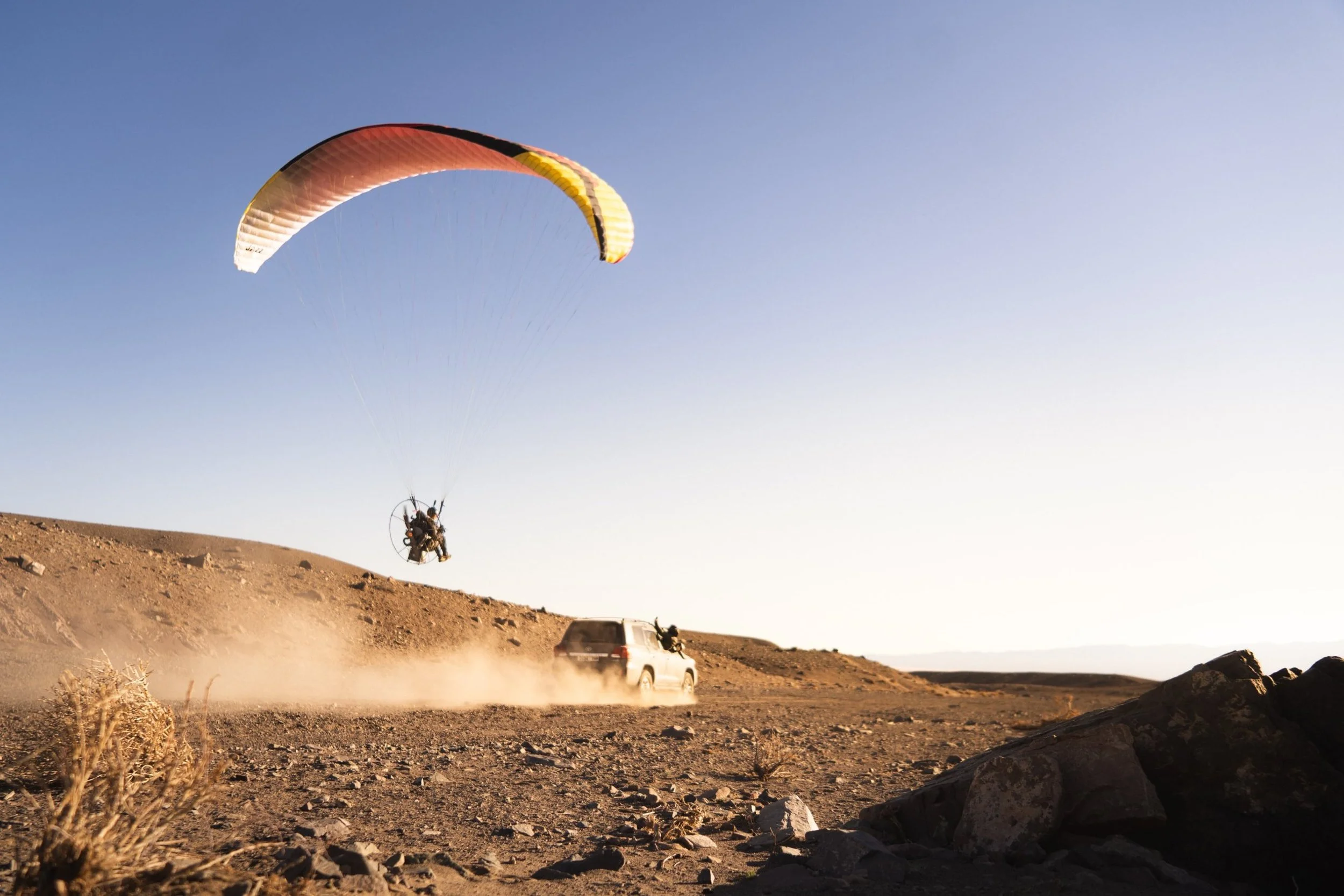 Paramotor pilot flying low behind the expedition support vehicle in the Mongolian desert