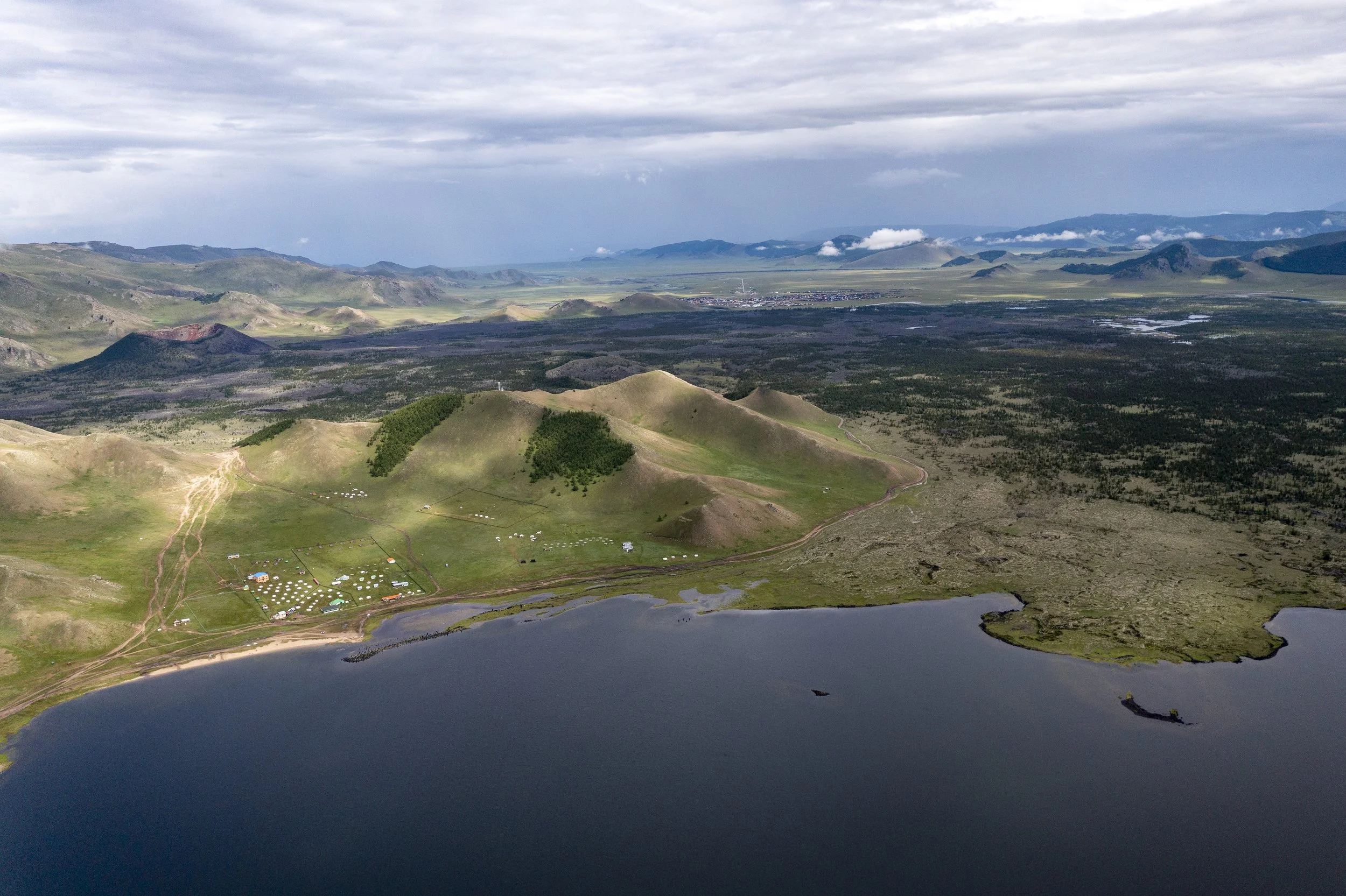 Aerial view of a mountainous landscape with a lake in the foreground, green hills, and a cloudy sky.