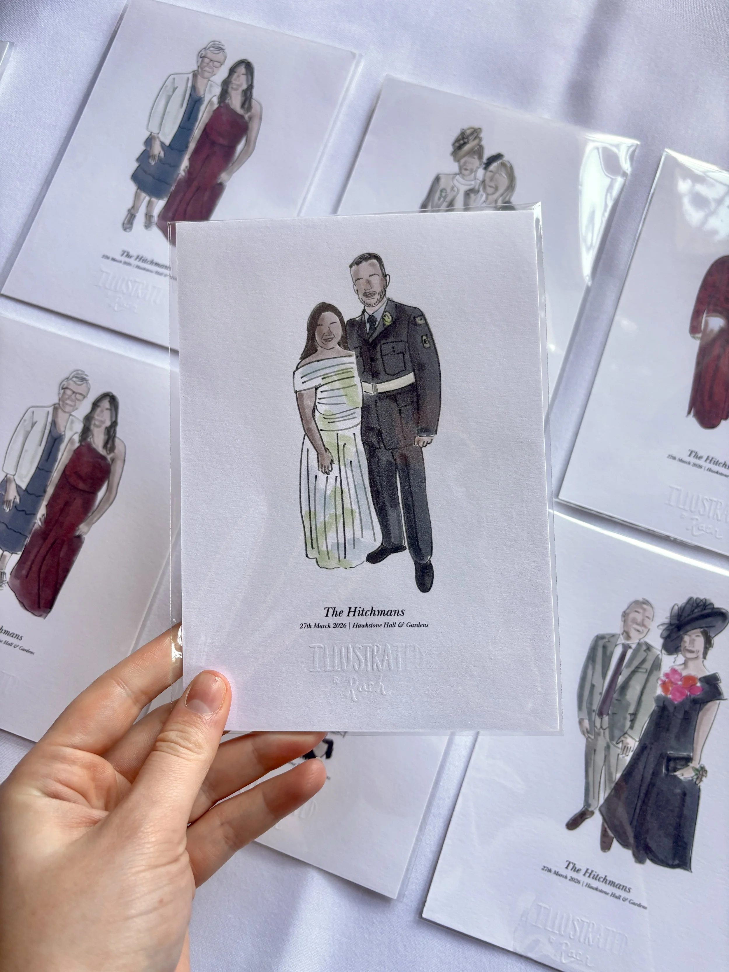 A hand holding a white paper with a watercolor illustration of a woman in a striped dress and a man in a military uniform, smiling. The paper is labeled 'The Hitchmans, 27th March 2026, Hawkstone Hall & Gardens.' Other similar illustrations are visib