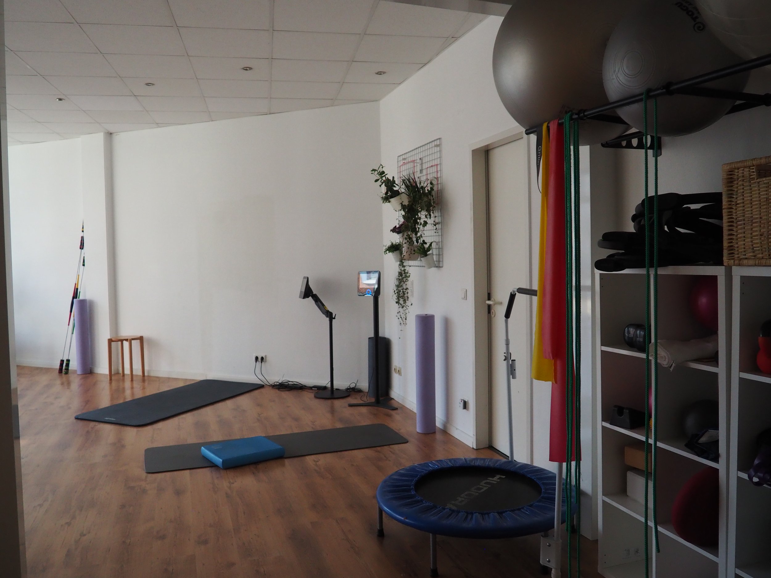 Ein Fitnessraum mit Yoga-Matten, Sprungtuch, Gymnastikstangen, Stühlen, Gymnastikbällen, Medizinbällen und einer Trampolin.