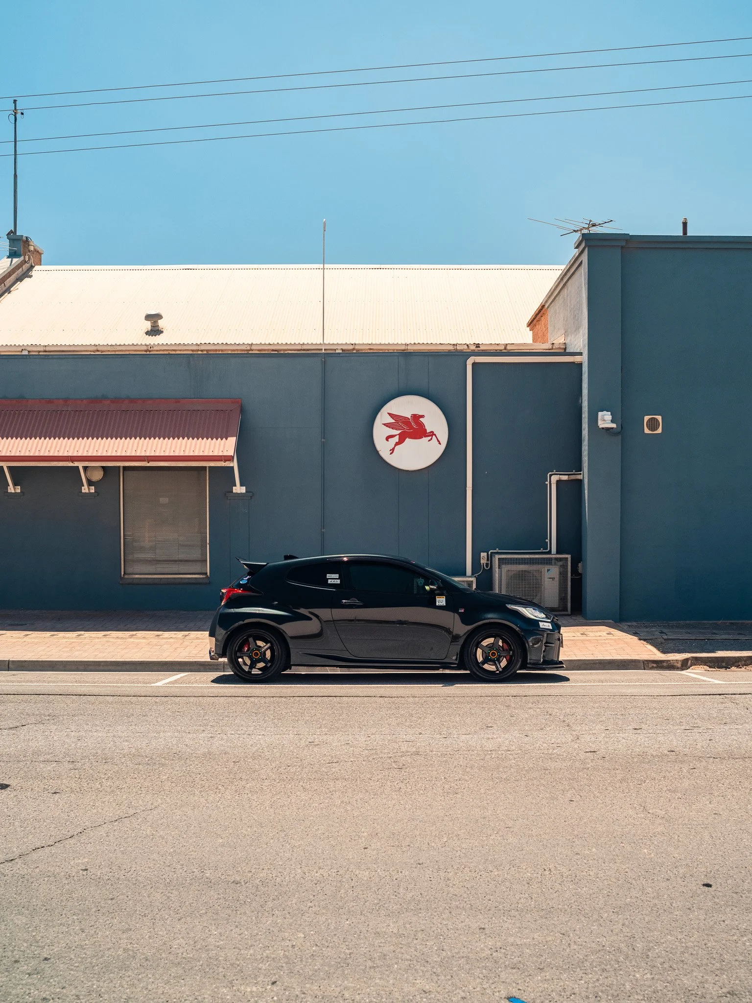 A black car parked on the side of the street in front of a blue building with a red Pegasus logo.