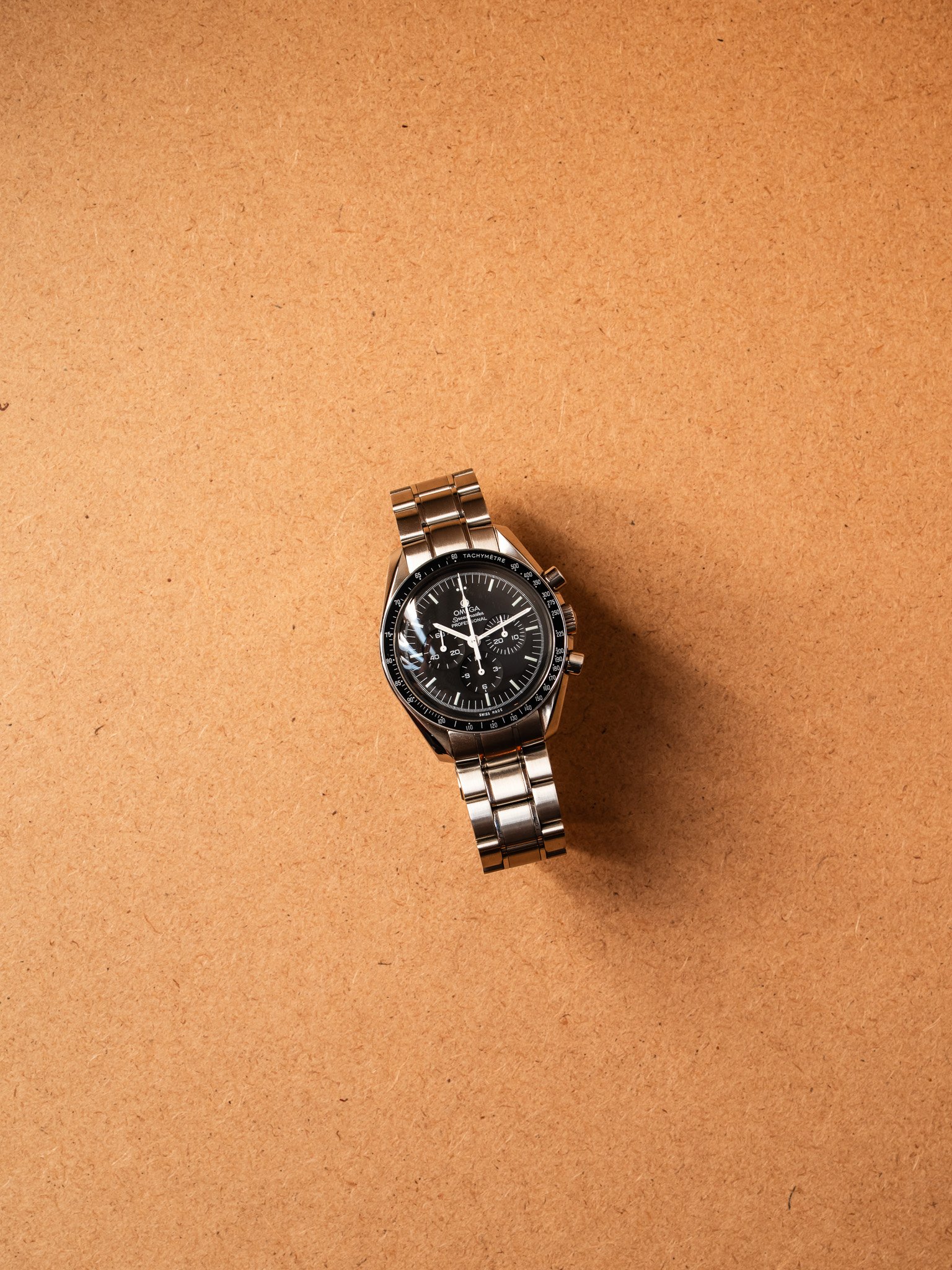 A silver wristwatch with a black dial and chronograph features placed on a brown surface.