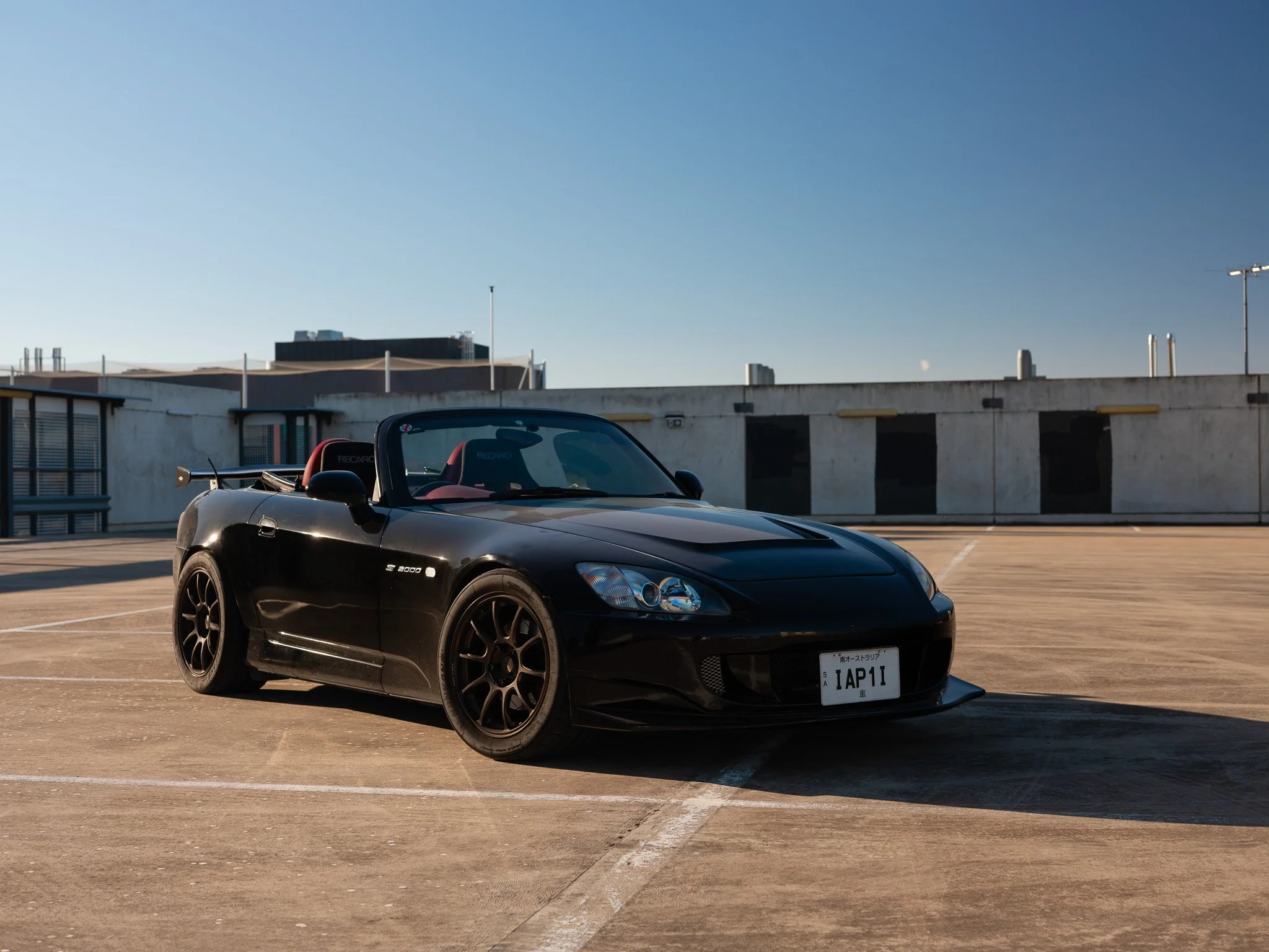 Black convertible sports car parked on rooftop parking lot under clear blue sky
