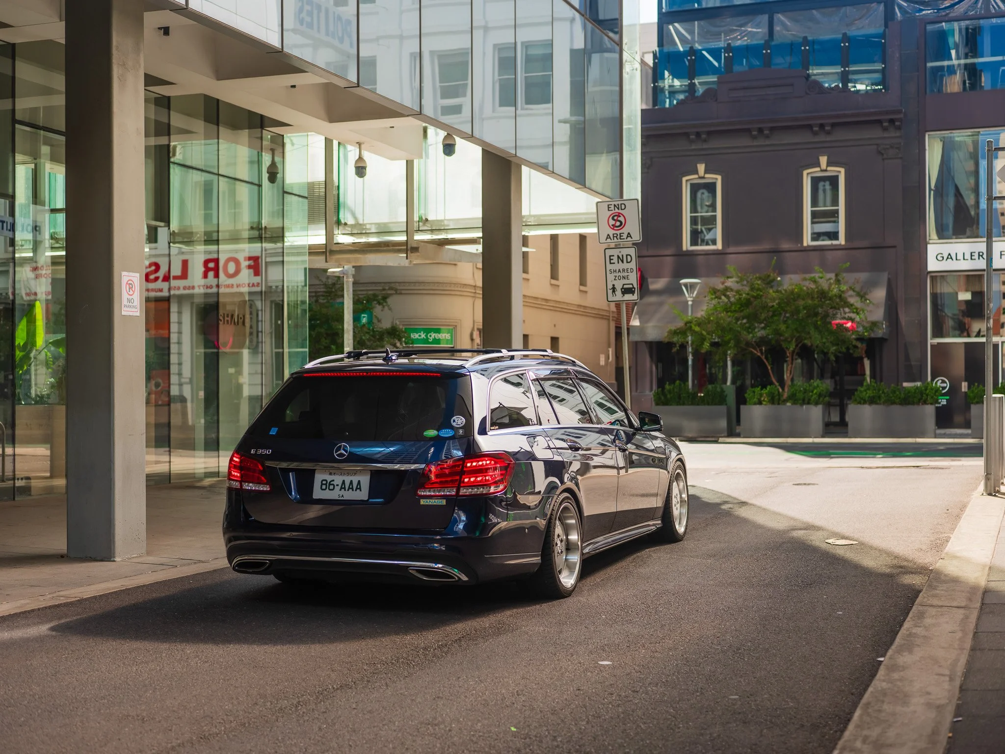 A black Mercedes-Benz E 350 wagon parked on a city street near a glass building with a sign indicating no parking in the area.