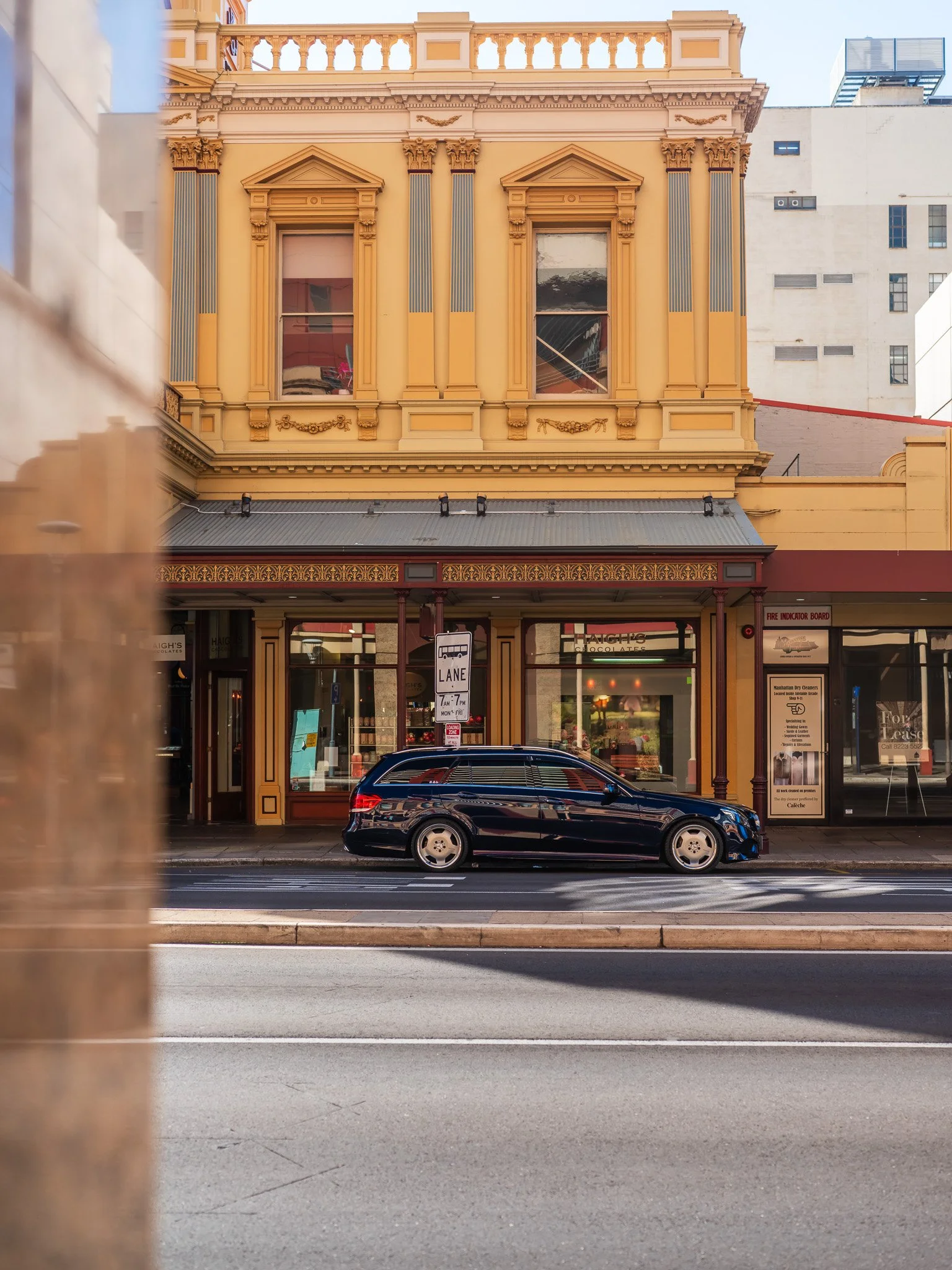 A historic building with ornate yellow facade and large windows, with a black station wagon car parked in front on a city street.