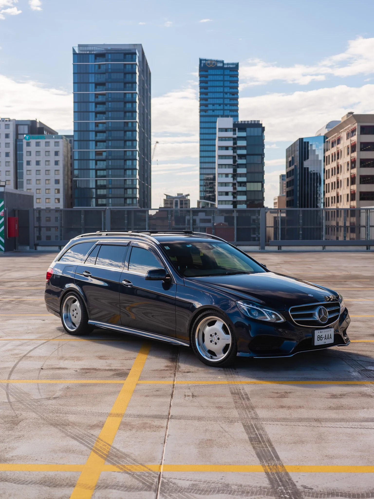 Black Mercedes-Benz station wagon parked on rooftop parking lot with city skyscrapers in the background.