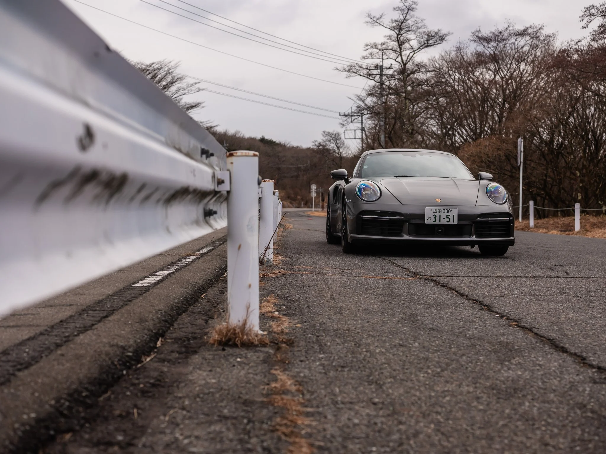 A black Porsche sports car parked on a rural road with a guardrail on the left and trees in the background.
