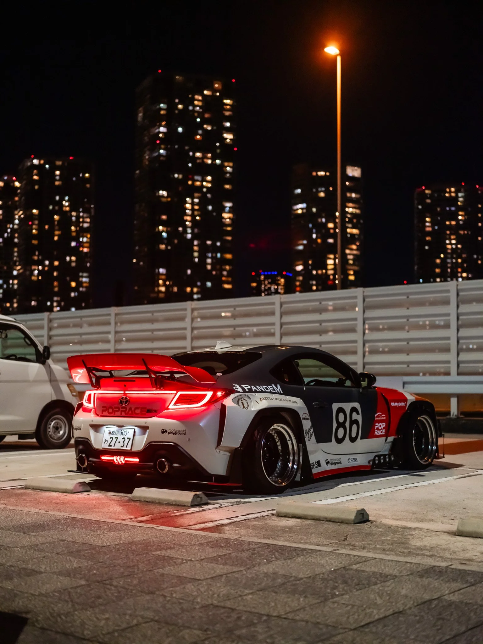 Night shot of a race car with the number 86 parked in an urban area with illuminated skyscrapers in the background