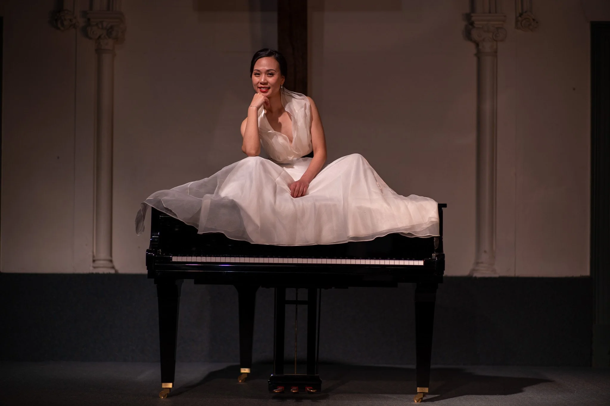 Woman in a white dress sitting on a black grand piano