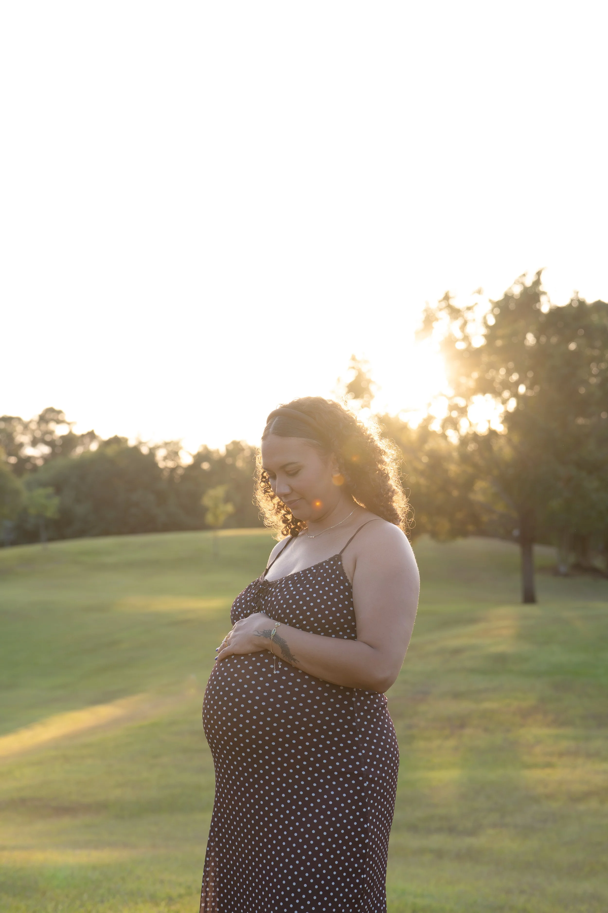 the woodlands mom admiring maternity belly during sunset in nature park