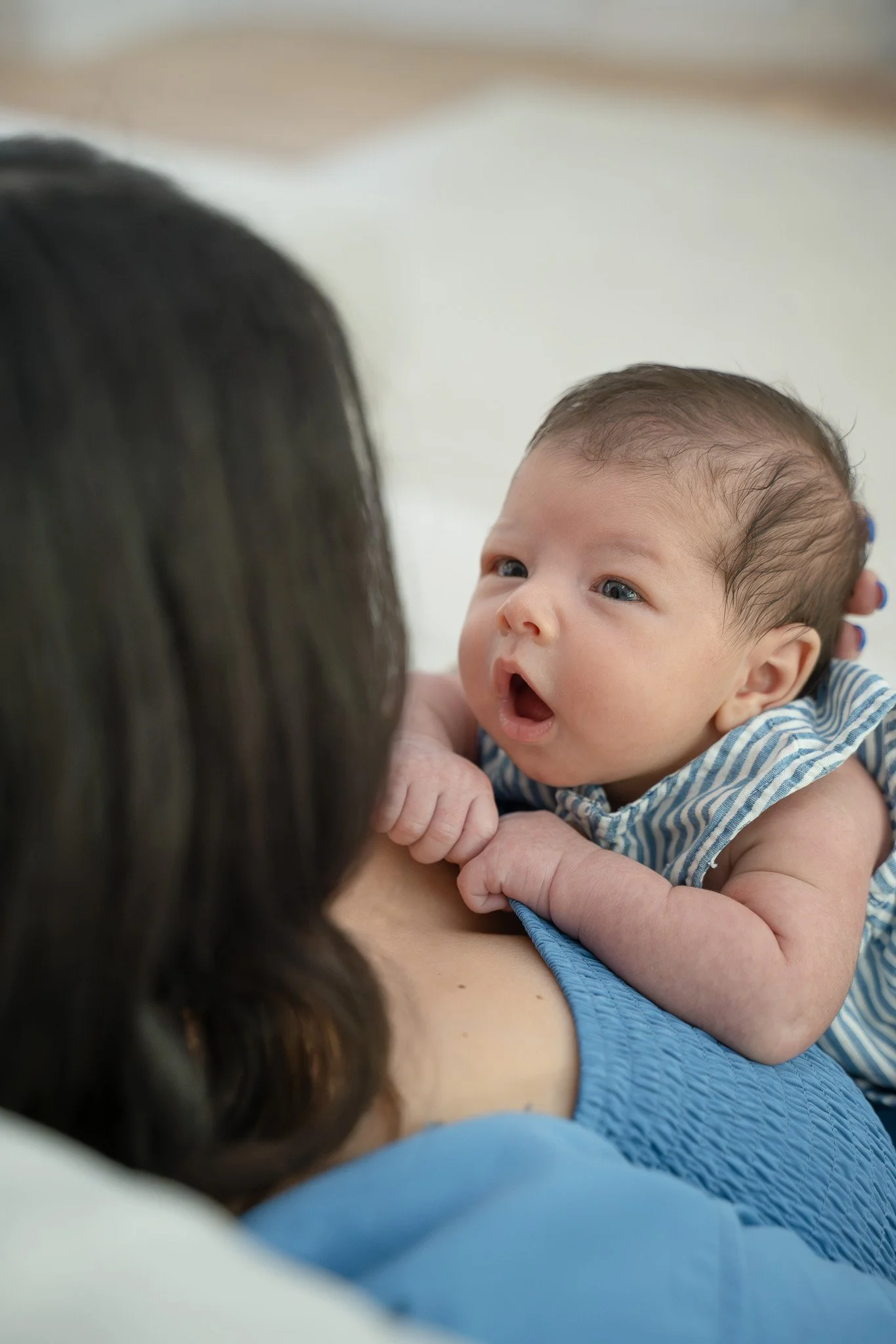 A baby with blue eyes and dark hair, dressed in a striped blue and white shirt, in their The Woodlands home.