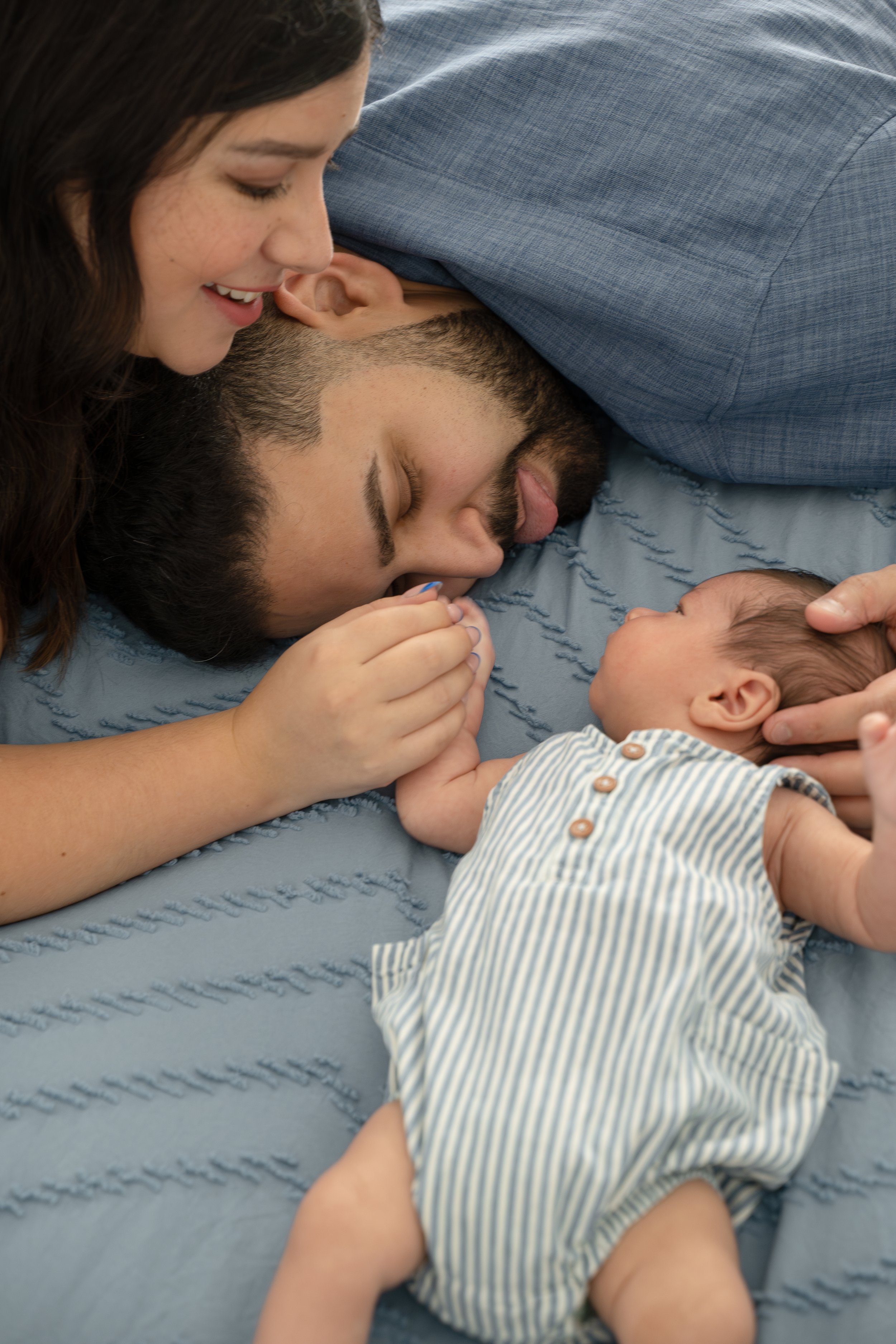 A woman and a man lying on a bed with the woman smiling and looking at a newborn baby who is lying on the bed, in their The Woodlands home.