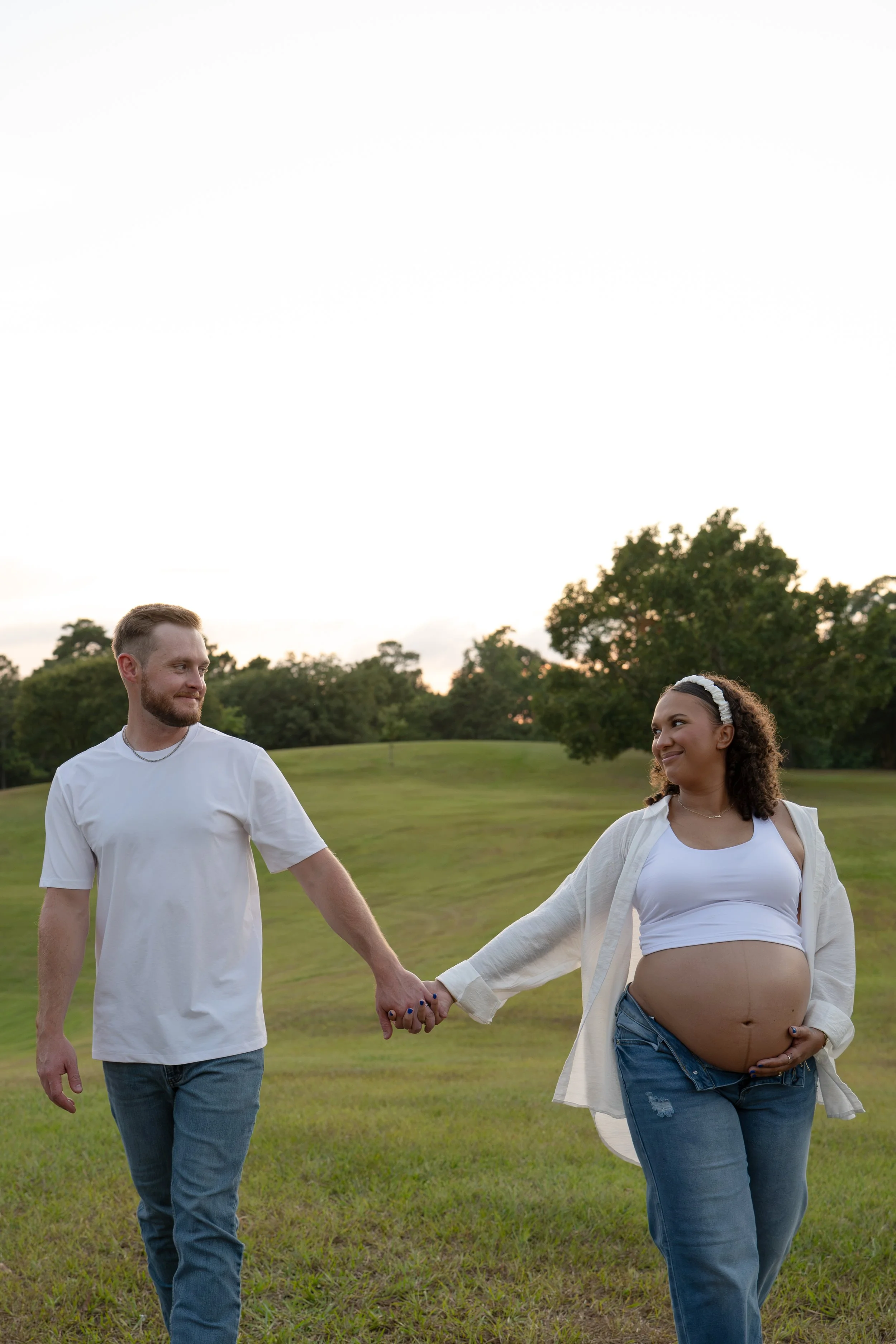 the woodlands couple walking and smiling in nature while mom holds pregnant belly