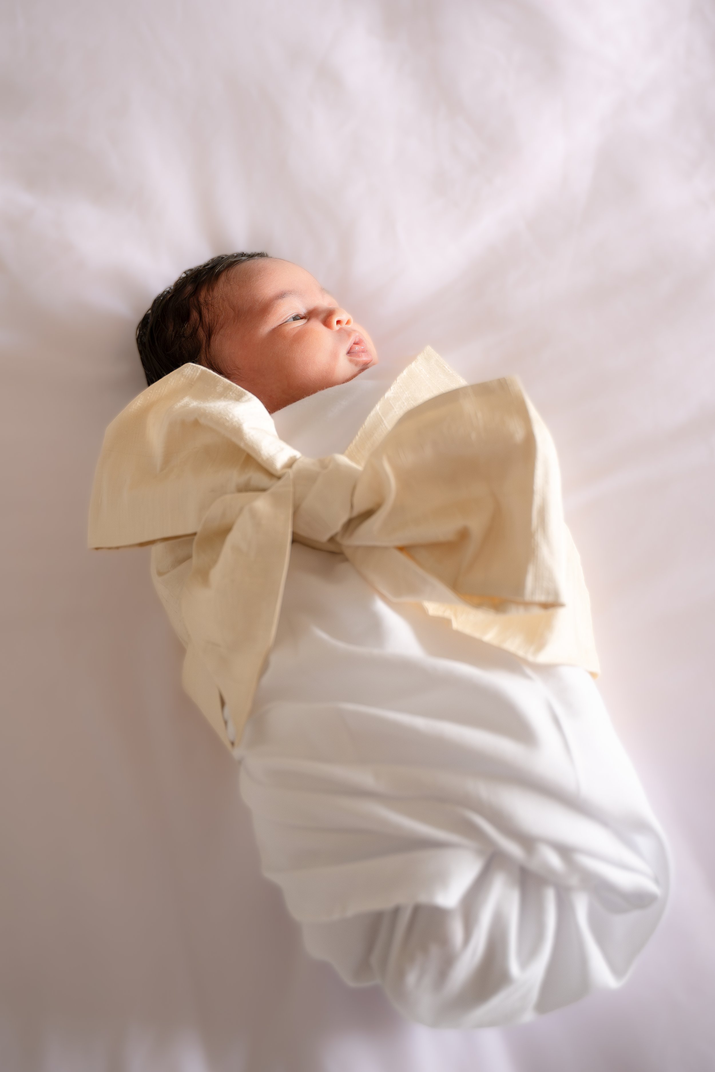 A newborn baby wrapped in a light-colored, silky cloth, lying on a white surface, in the Houston Ruby Postnatal. 