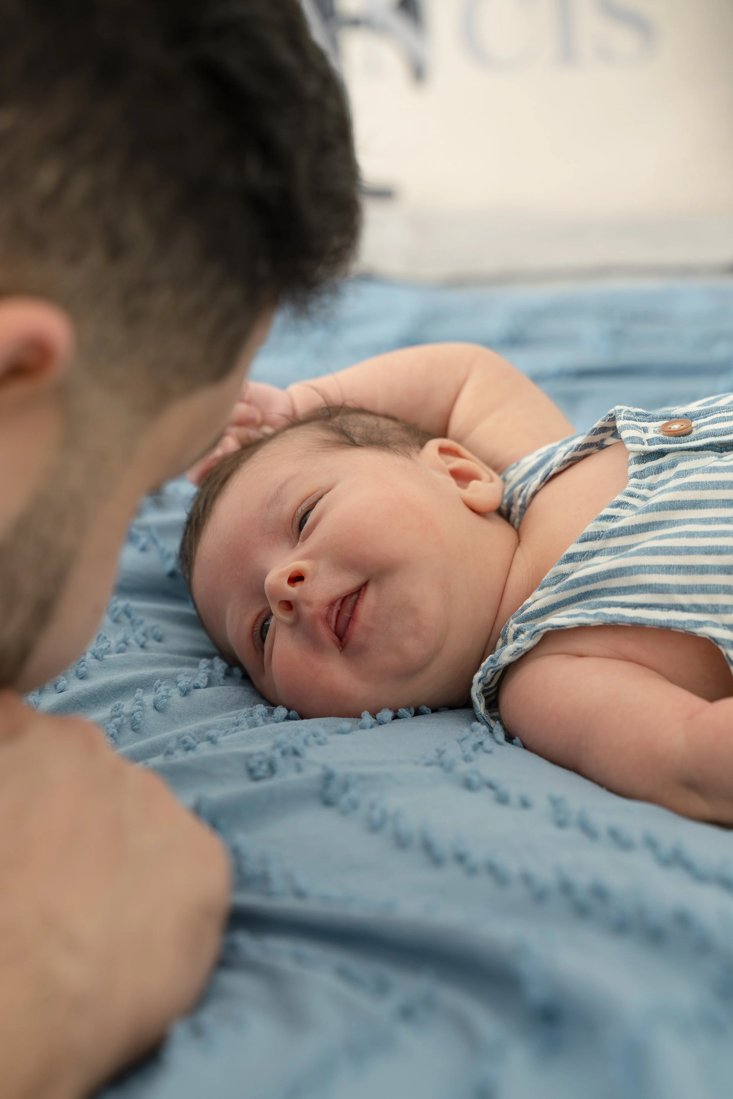 A man and a baby lying on a blue blanket. The baby is smiling while looking at the man, who is partially visible and looking at the baby, in their The Woodlands home.