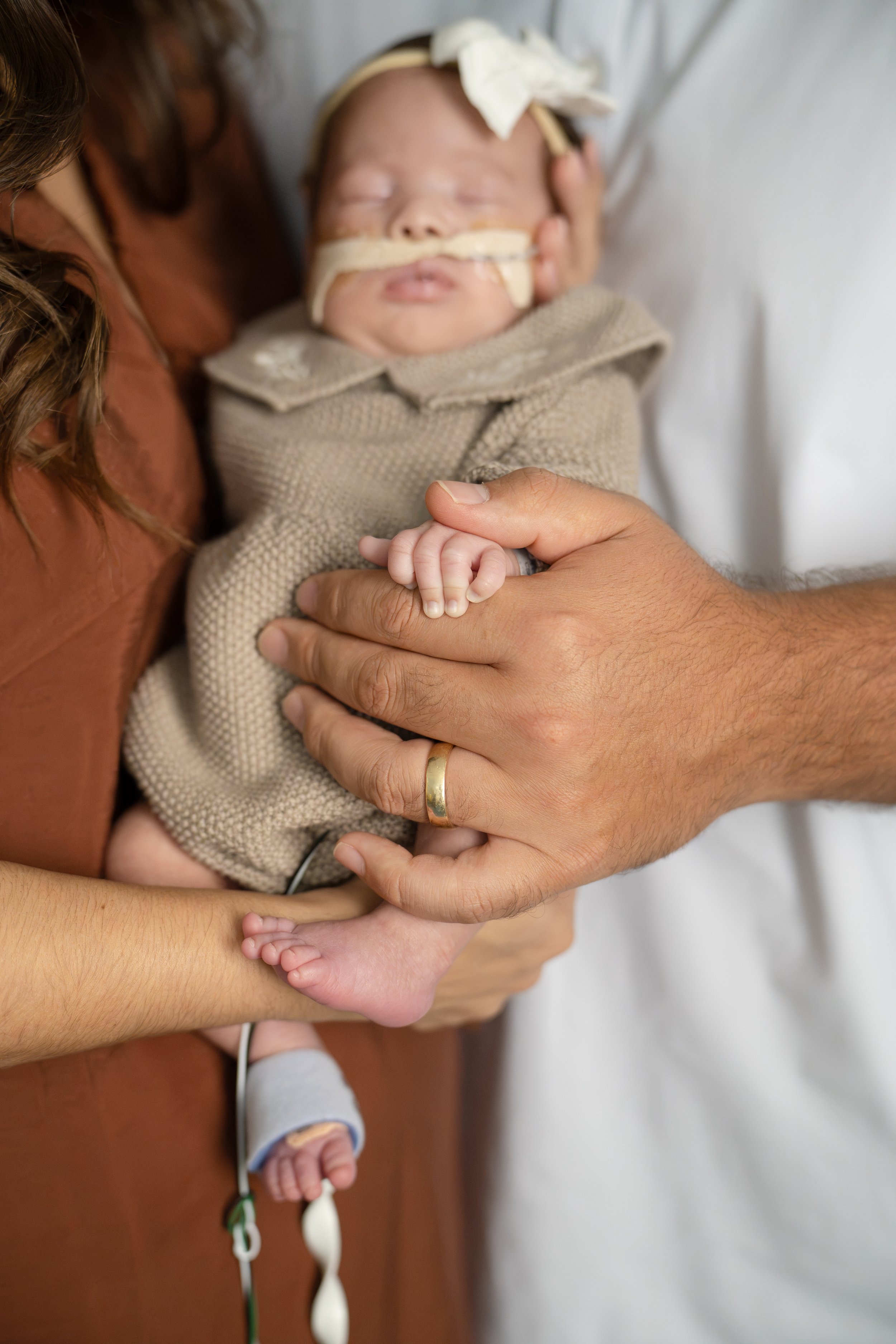 A newborn baby is being held by an adult around the chest, with the baby's head resting on the adult's shoulder at Houston medical center.