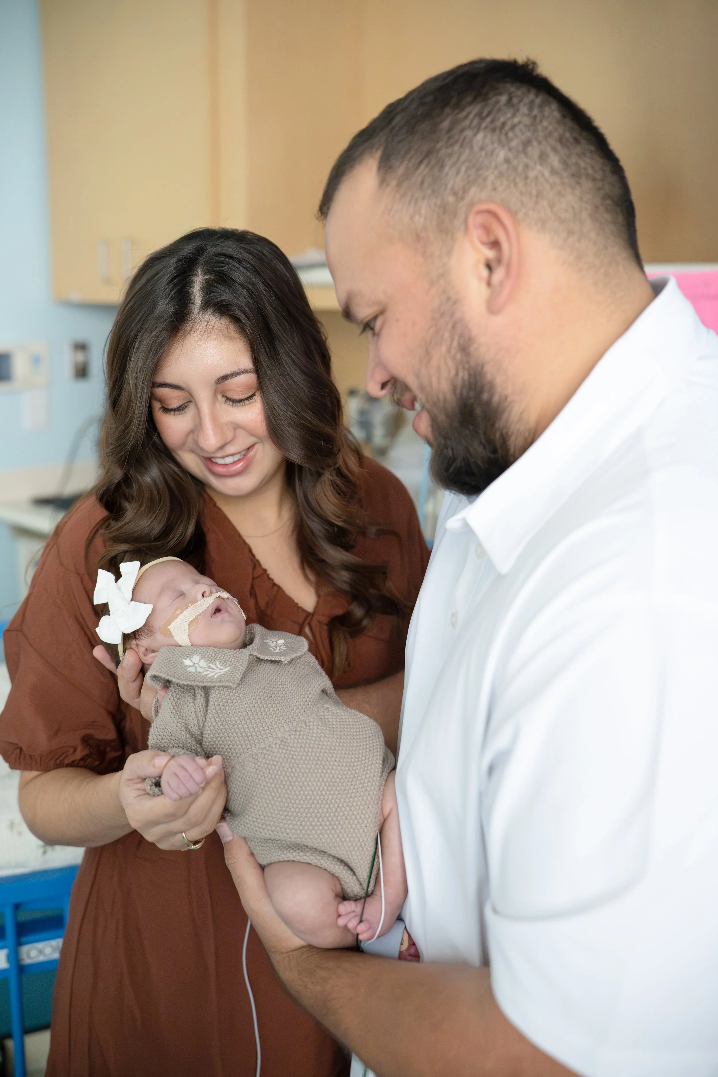 A woman holding a newborn baby while a man in a white shirt looks at the baby in a hospital room at Houston medical center.