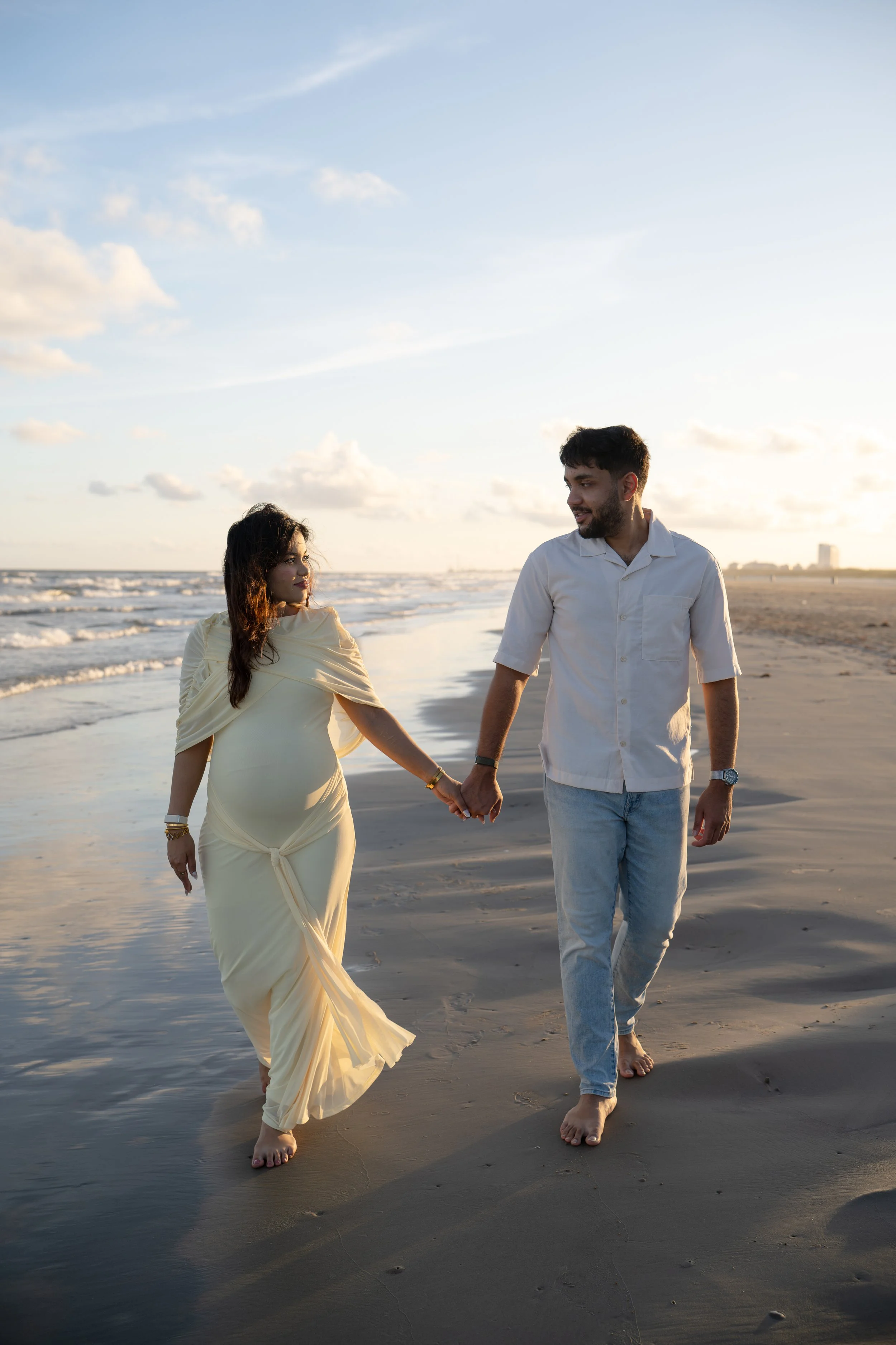galveston beach sunset maternity session with couple walking on the beach and maternity belly in yellow dress