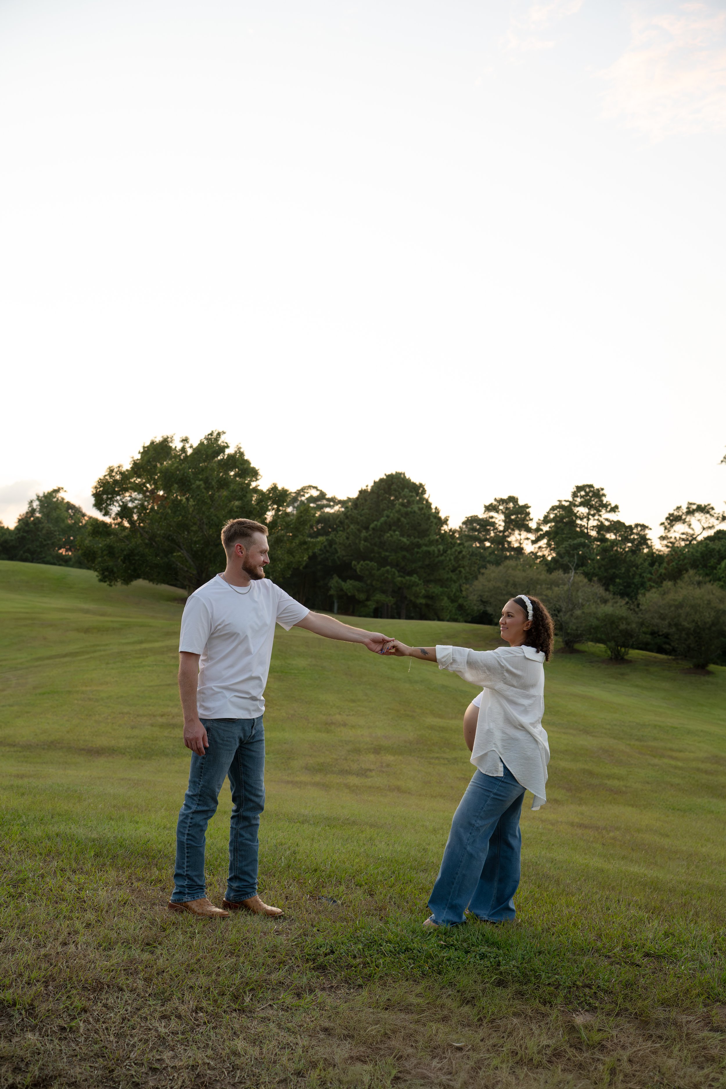 the woodlands couple holding hands while pregnant belly is showing in nature park