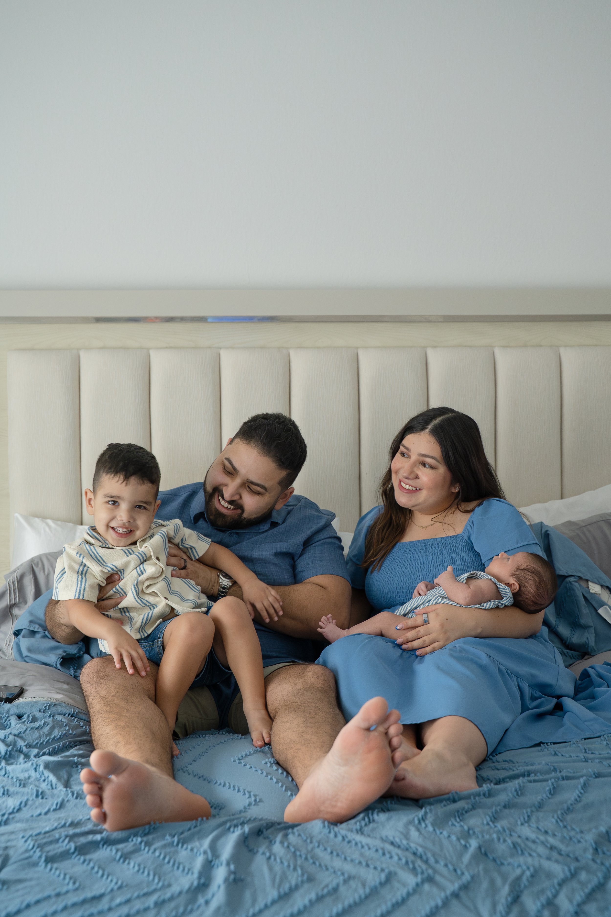 A family of five sitting on a bed, smiling and enjoying each other's company, in their The Woodlands home.
