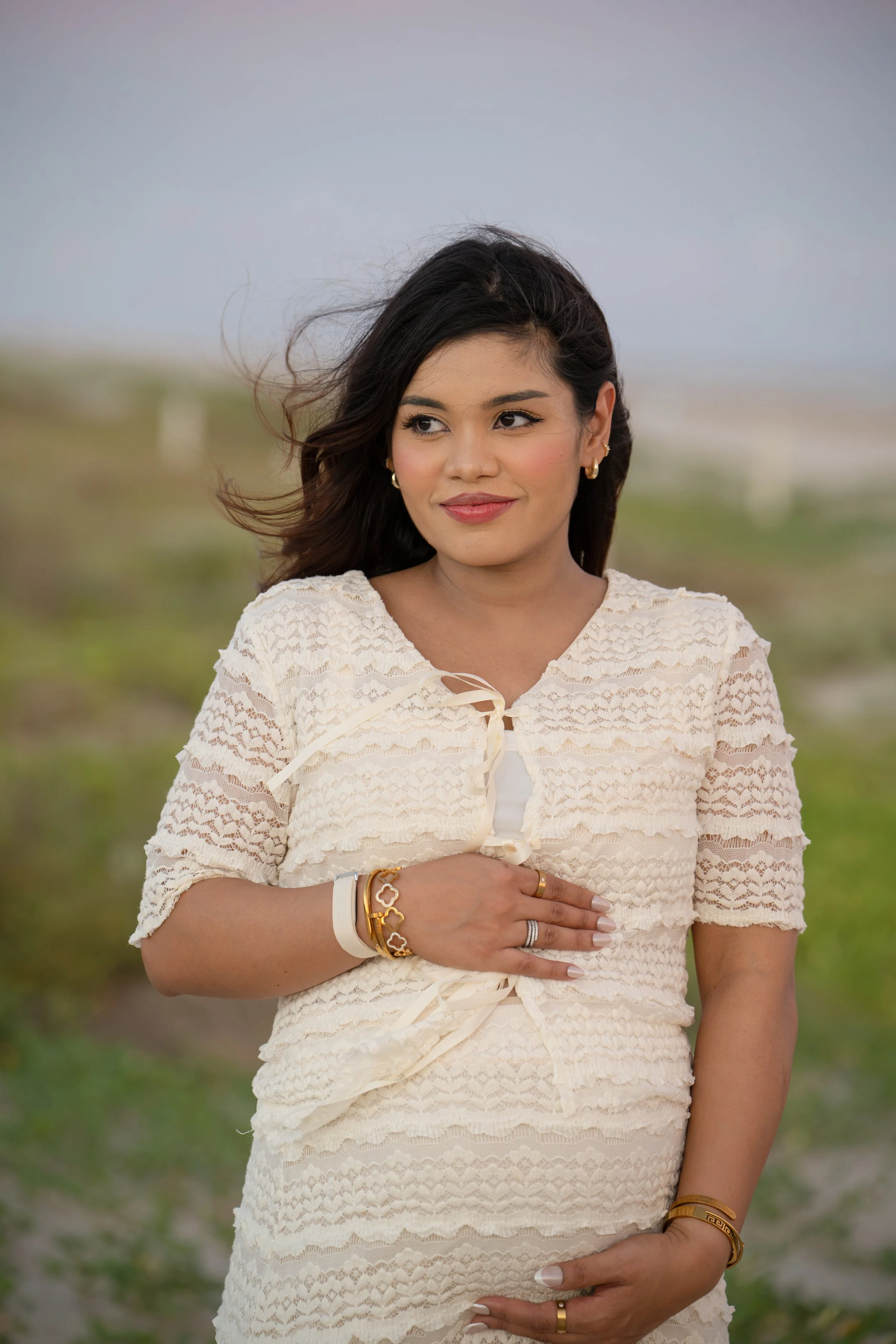 houston mom embracing maternity belly and smiling while at the beach at sunset